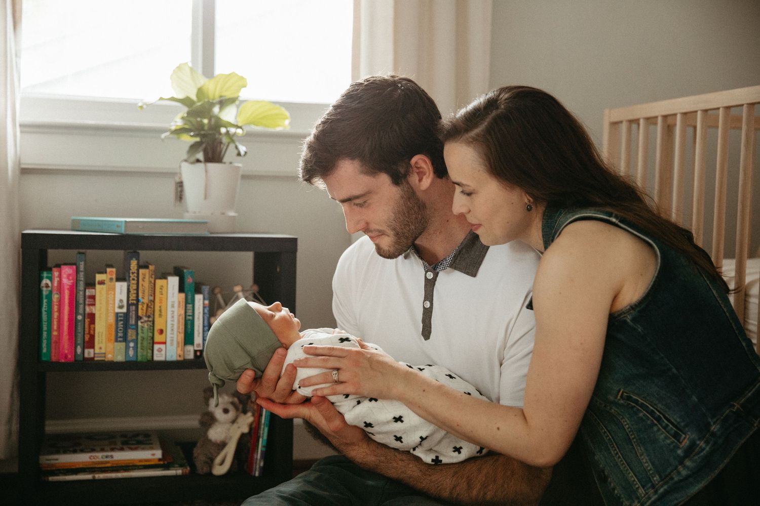 A couple bonds with their newborn baby near a bookshelf with yellow flowers.