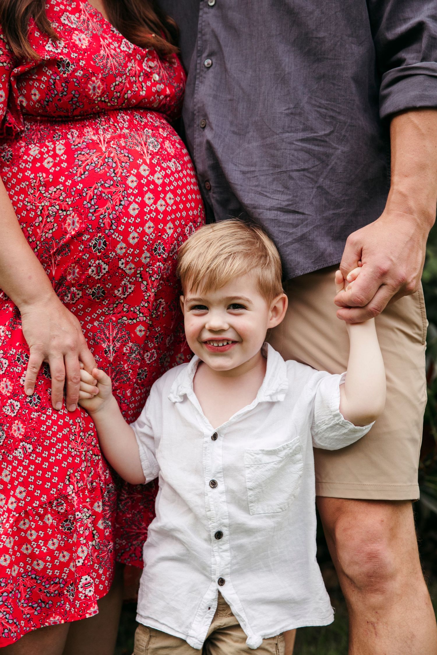 A family portrait showing a couple in casual attire holding hands with their small child.