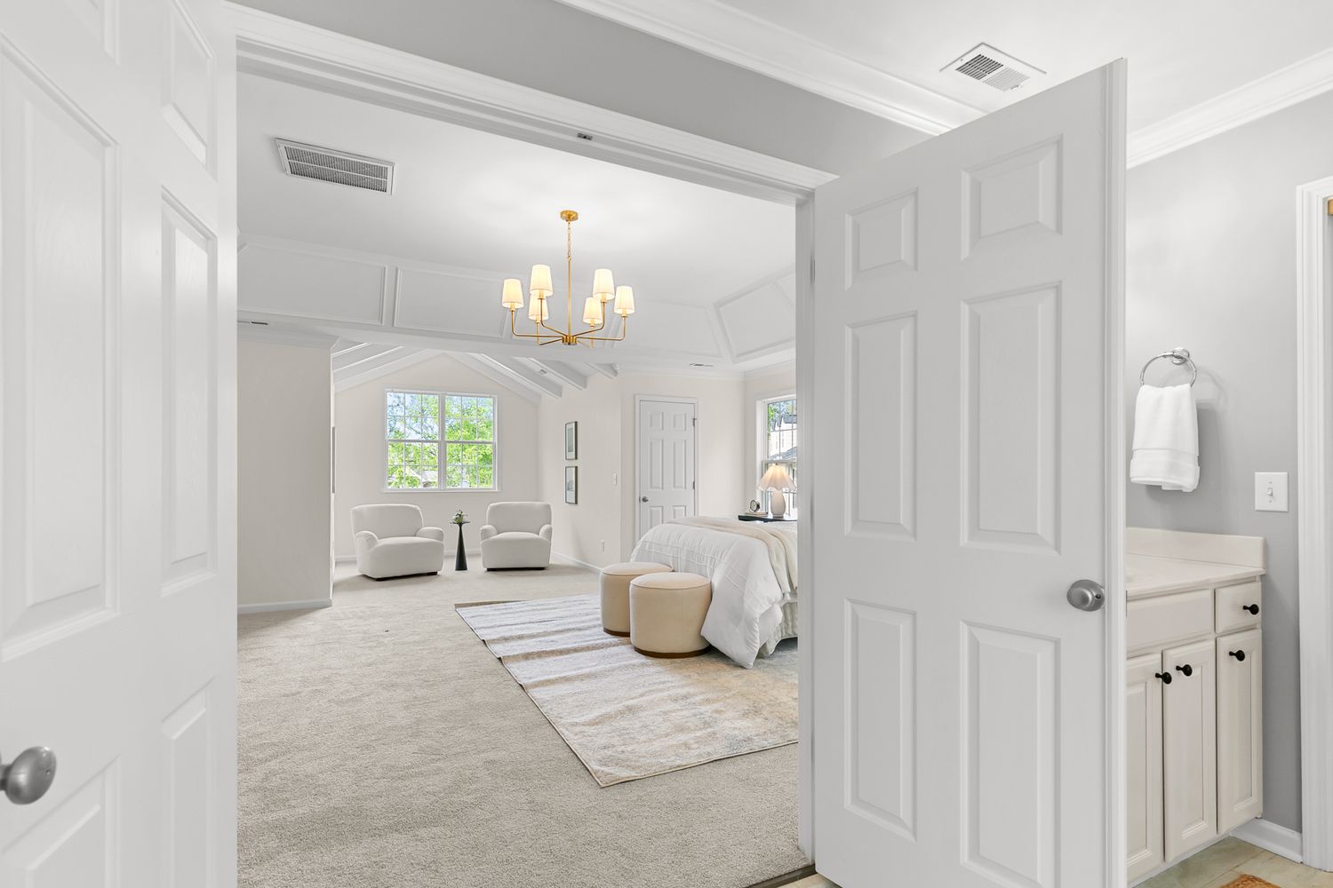 Elegant master bedroom suite with chandelier, arched doorways, neutral carpet, and an en-suite bathroom vanity visible through open door.