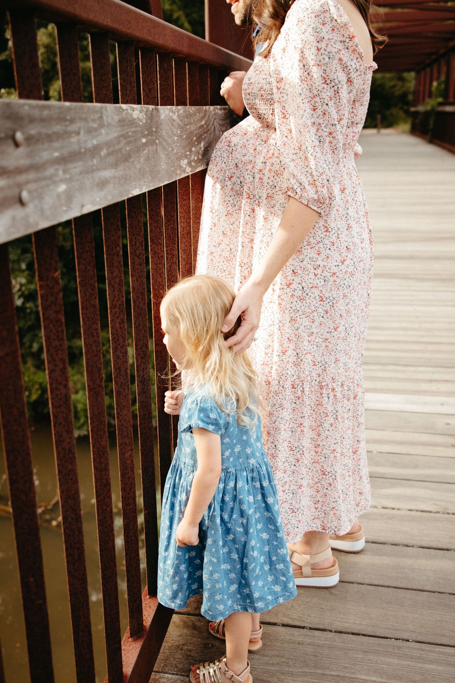 Mother and child walking on wooden bridge with matching floral dresses.