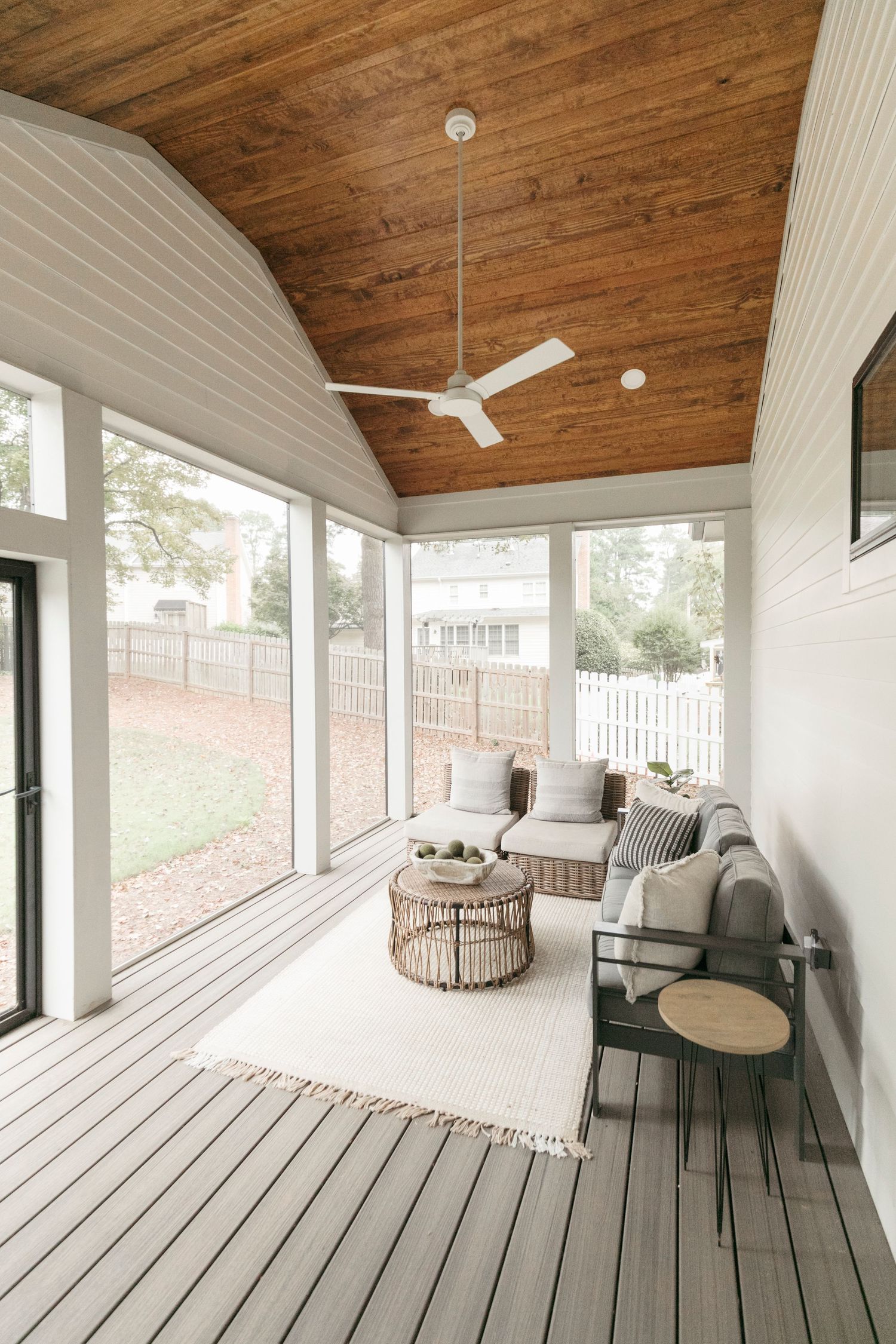 Covered deck with wooden ceiling, white walls, and gray flooring furnished with comfortable outdoor seating.