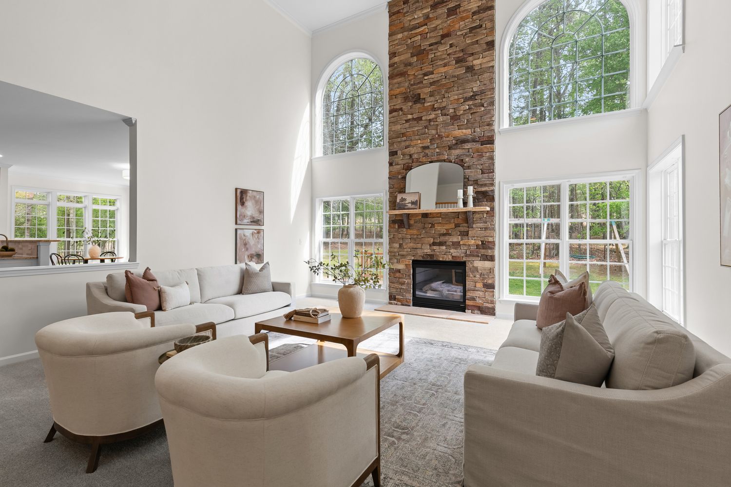 Bright living room with high ceilings, arched windows, white sofas, and a stone fireplace.