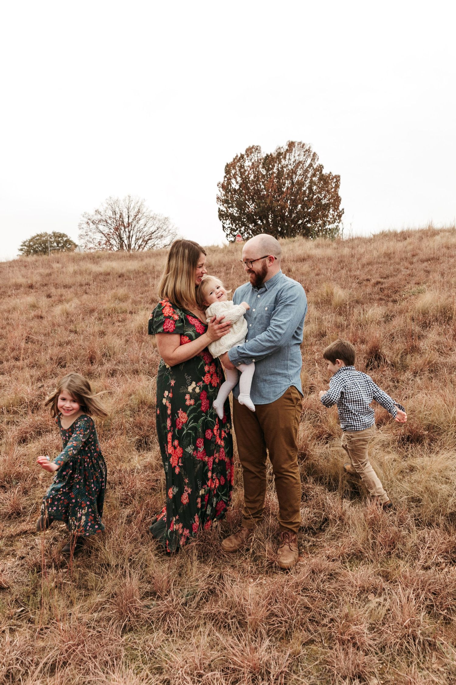 Family enjoying an outdoor photo session on a golden hillside with children playing in the background.