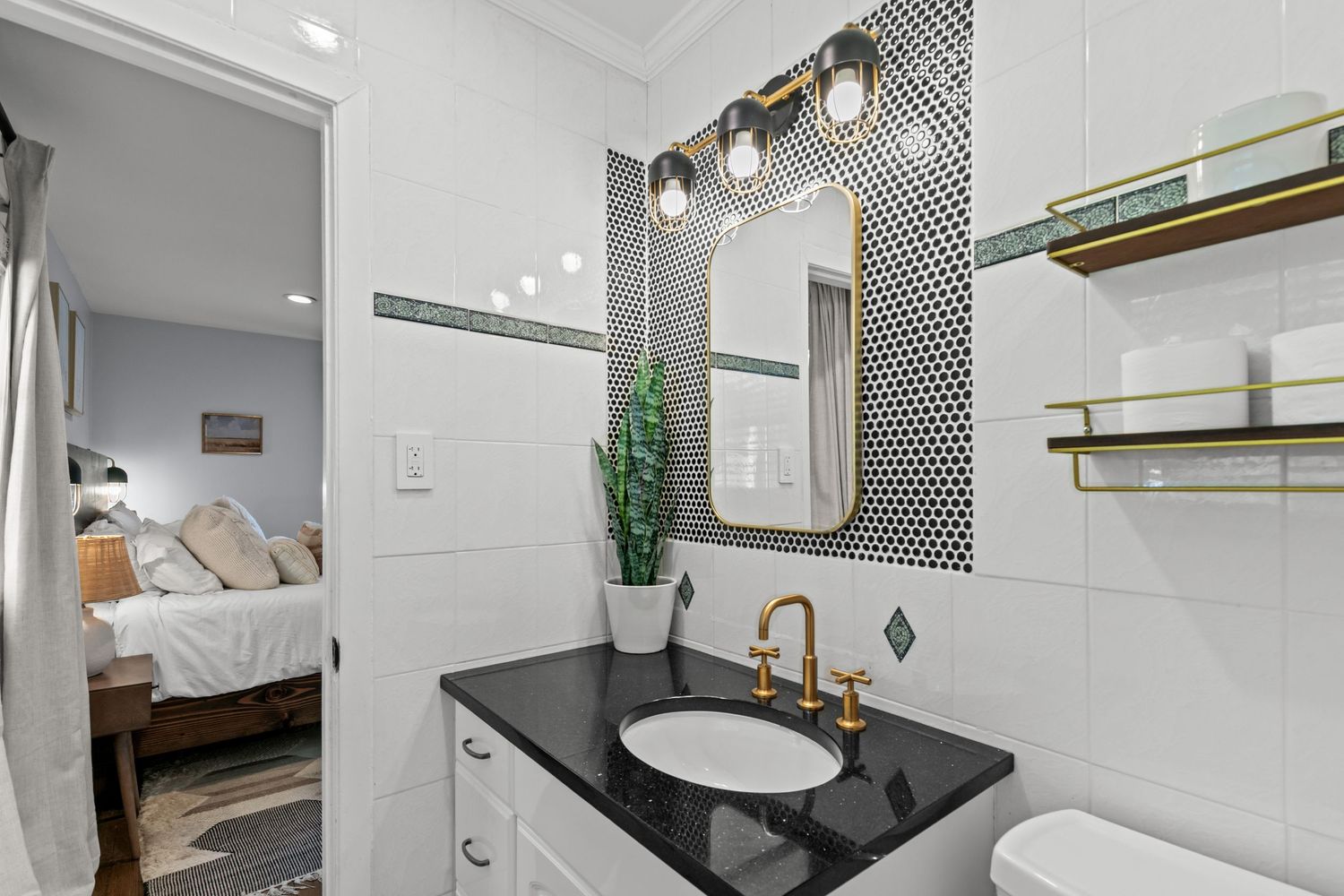 Modern bathroom with black penny tile accent wall, gold fixtures, black granite vanity, and open view to bedroom.