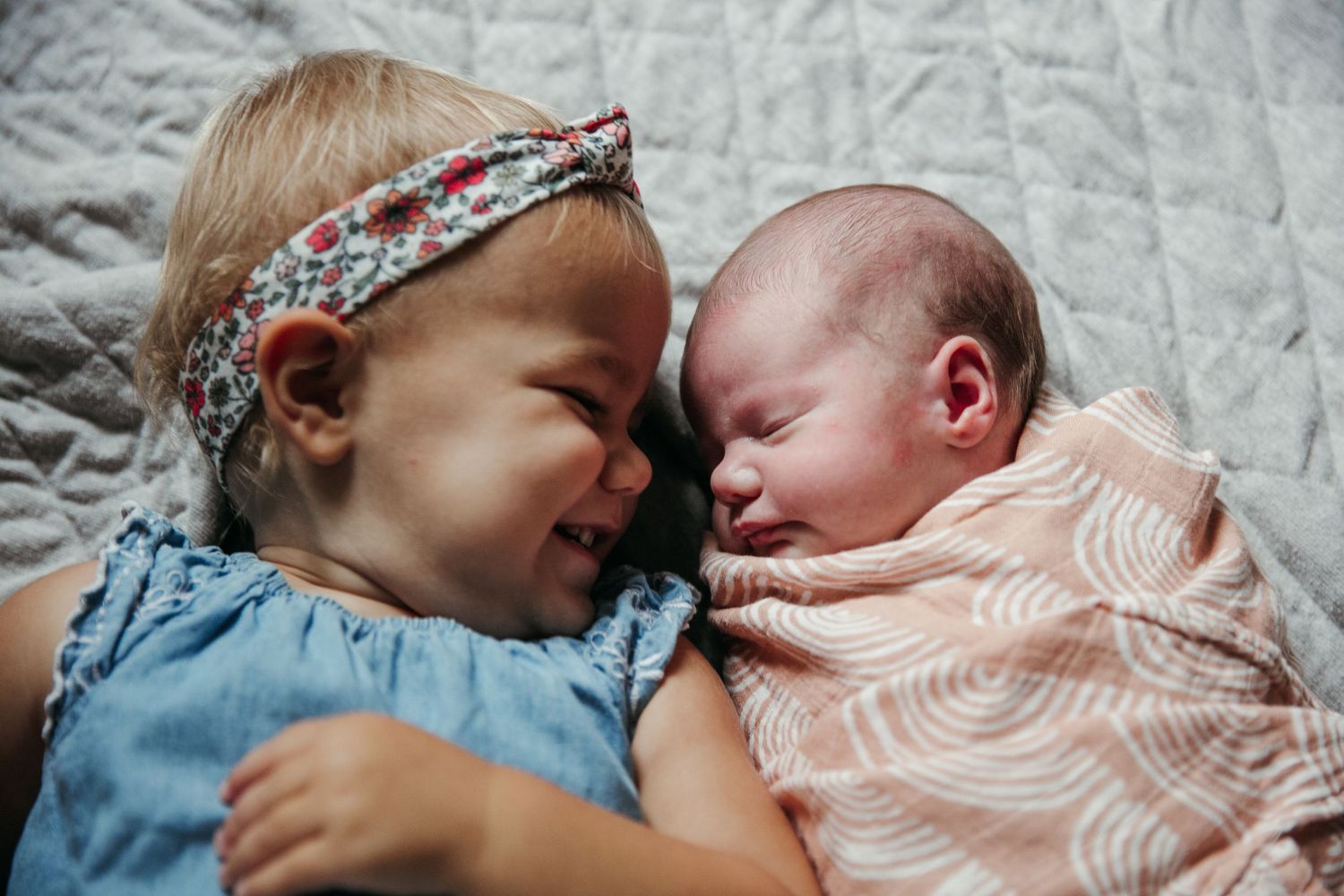 Sweet sibling bonding moments with newborn baby on white bedding.