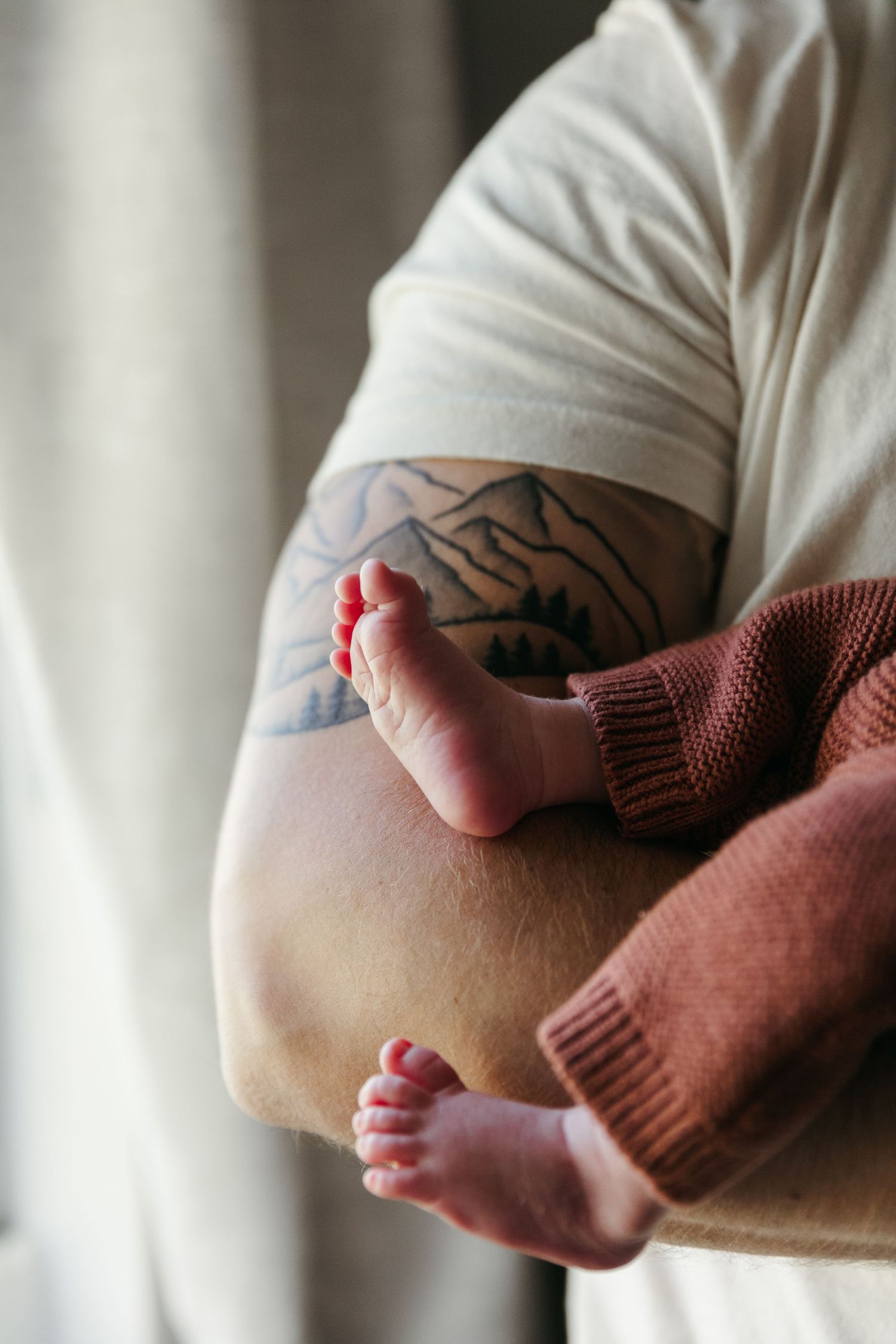 Close-up series showing tiny baby feet resting against someone's tattooed arm.