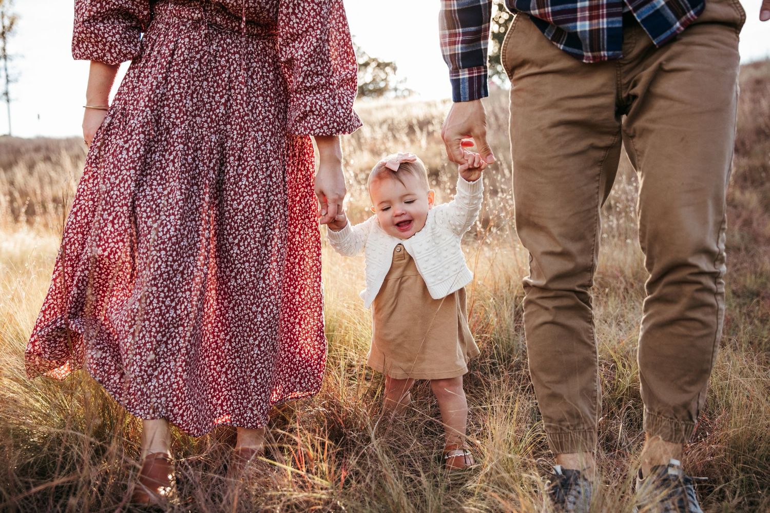 Small child stands between parents wearing complementary outfits in tall grass.
