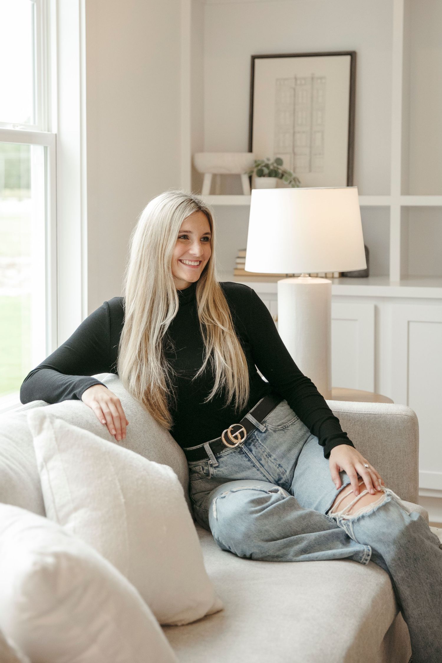 Casual lifestyle portrait showing off fashion styling with black sweater and Gucci belt on a light gray couch.