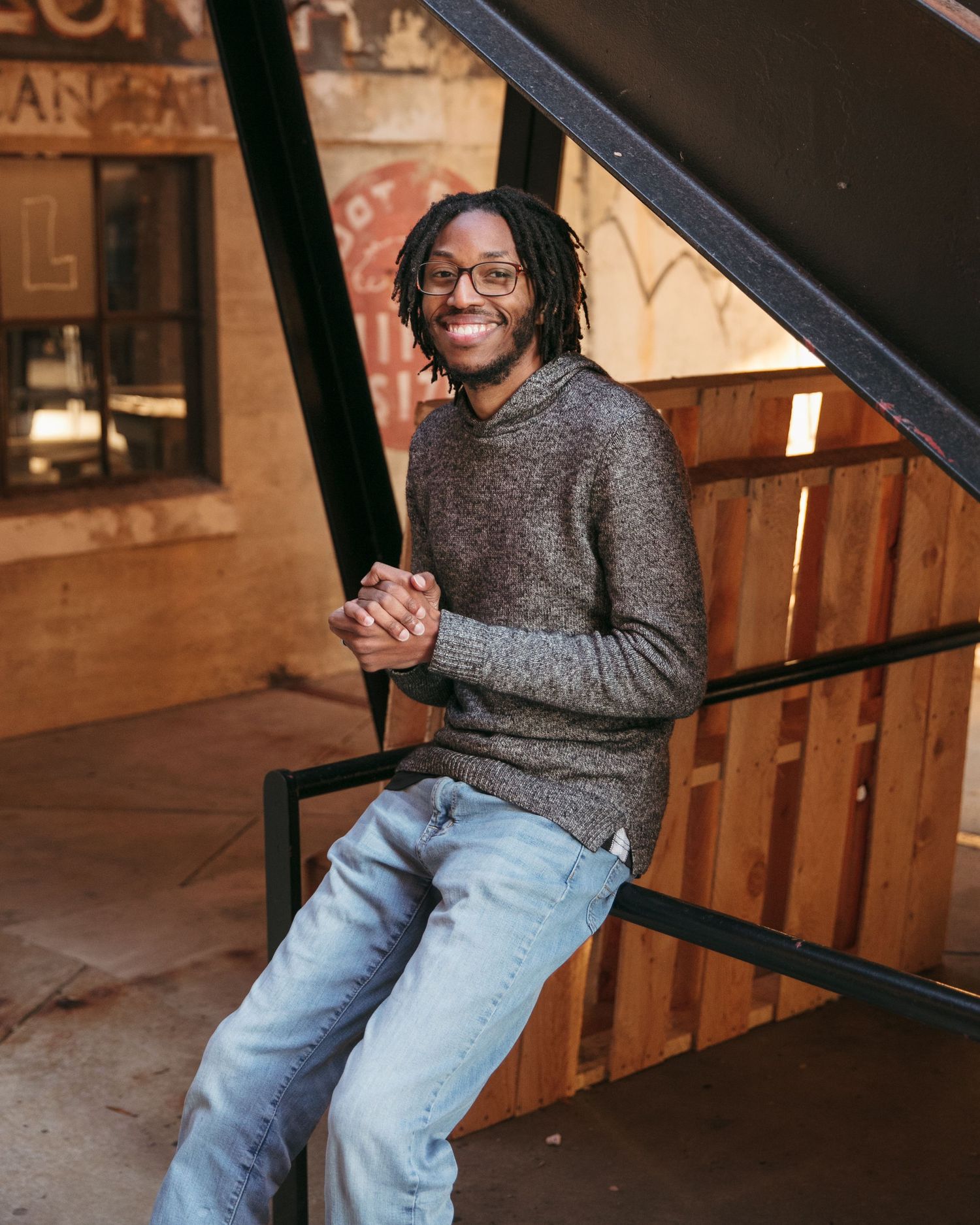 Person in gray sweater and jeans sitting on wooden stairs.