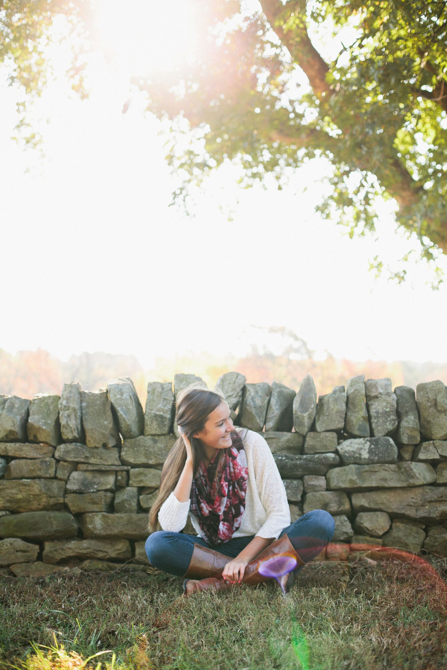 Candid outdoor portrait by rustic stone wall with autumn sunlight filtering through trees.