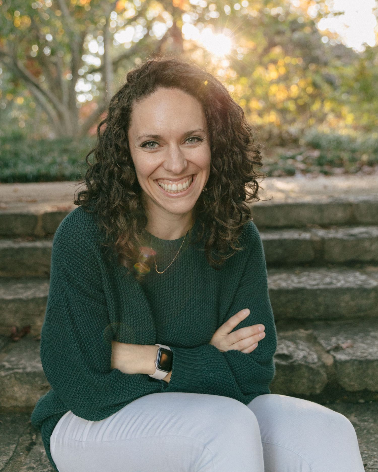 Sunset portrait series on stone steps wearing a dark green sweater and light colored pants.