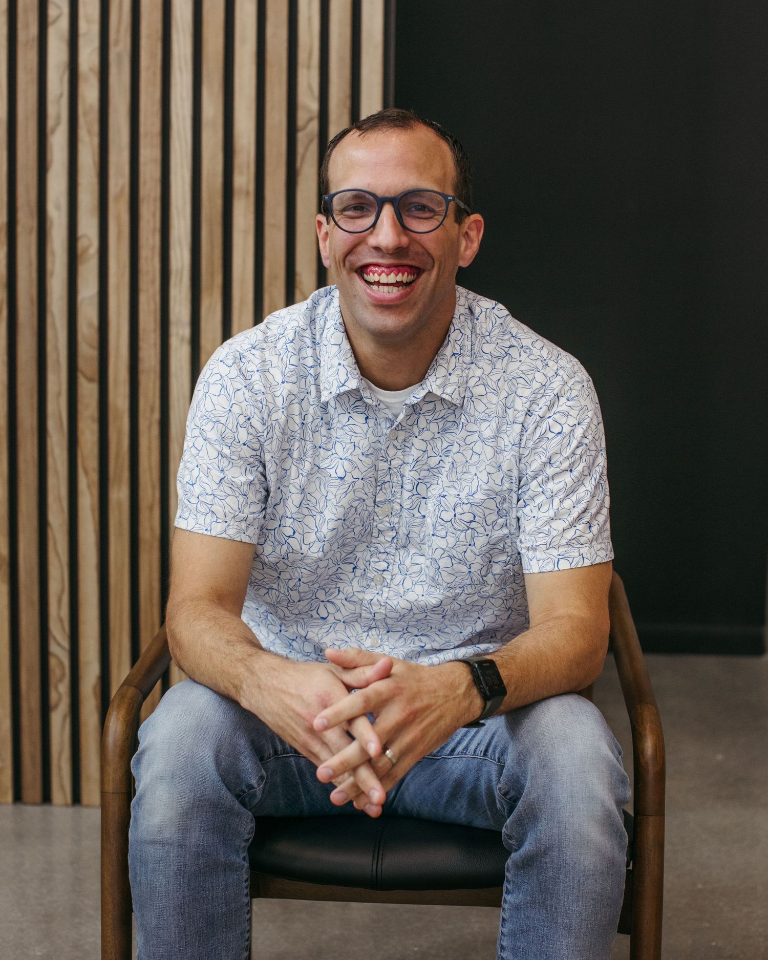 Candid shots of person in gray patterned shirt and jeans sitting relaxed against wooden wall panels.