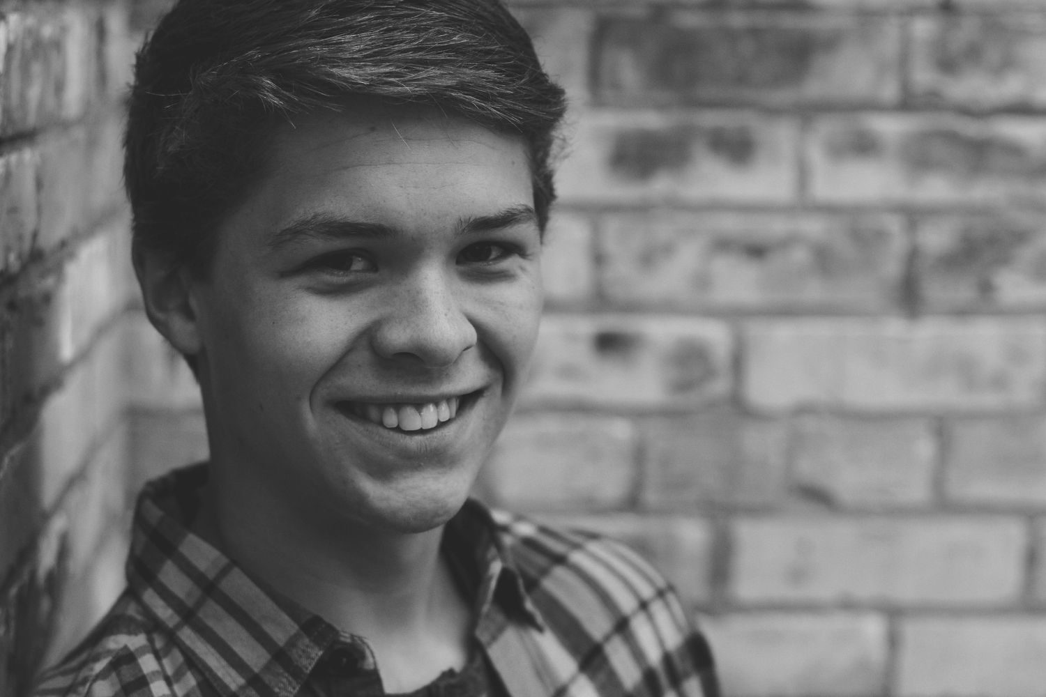 Close up black and white portrait against brick wall with natural smile.