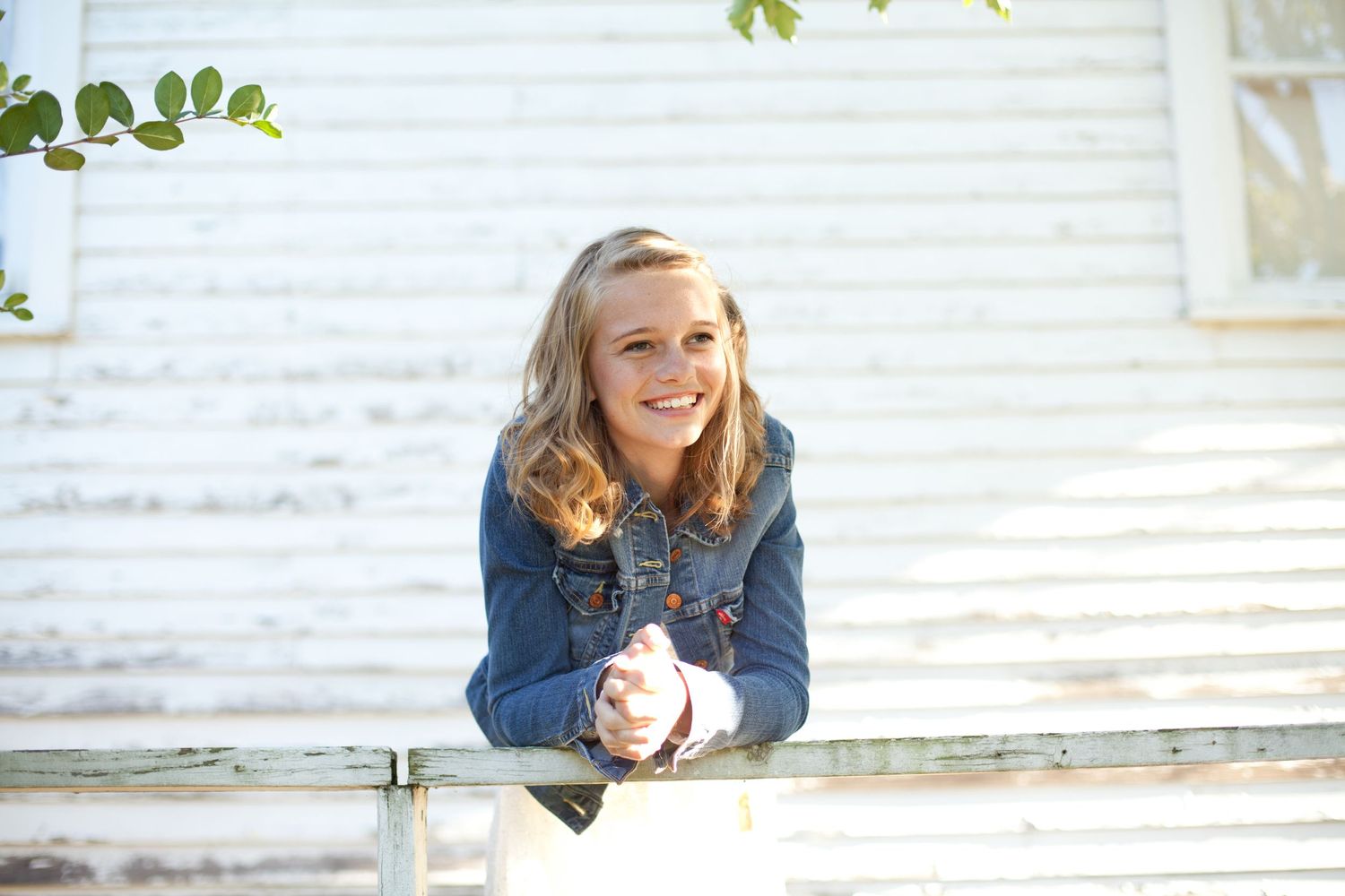 A casual outdoor portrait on a rustic white porch with green foliage in the background.