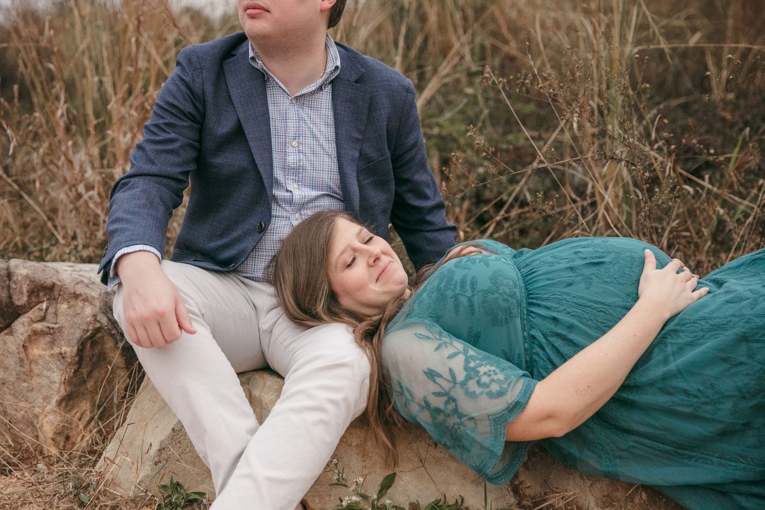A couple relaxes in casual attire among tall grass during an outdoor photo session.