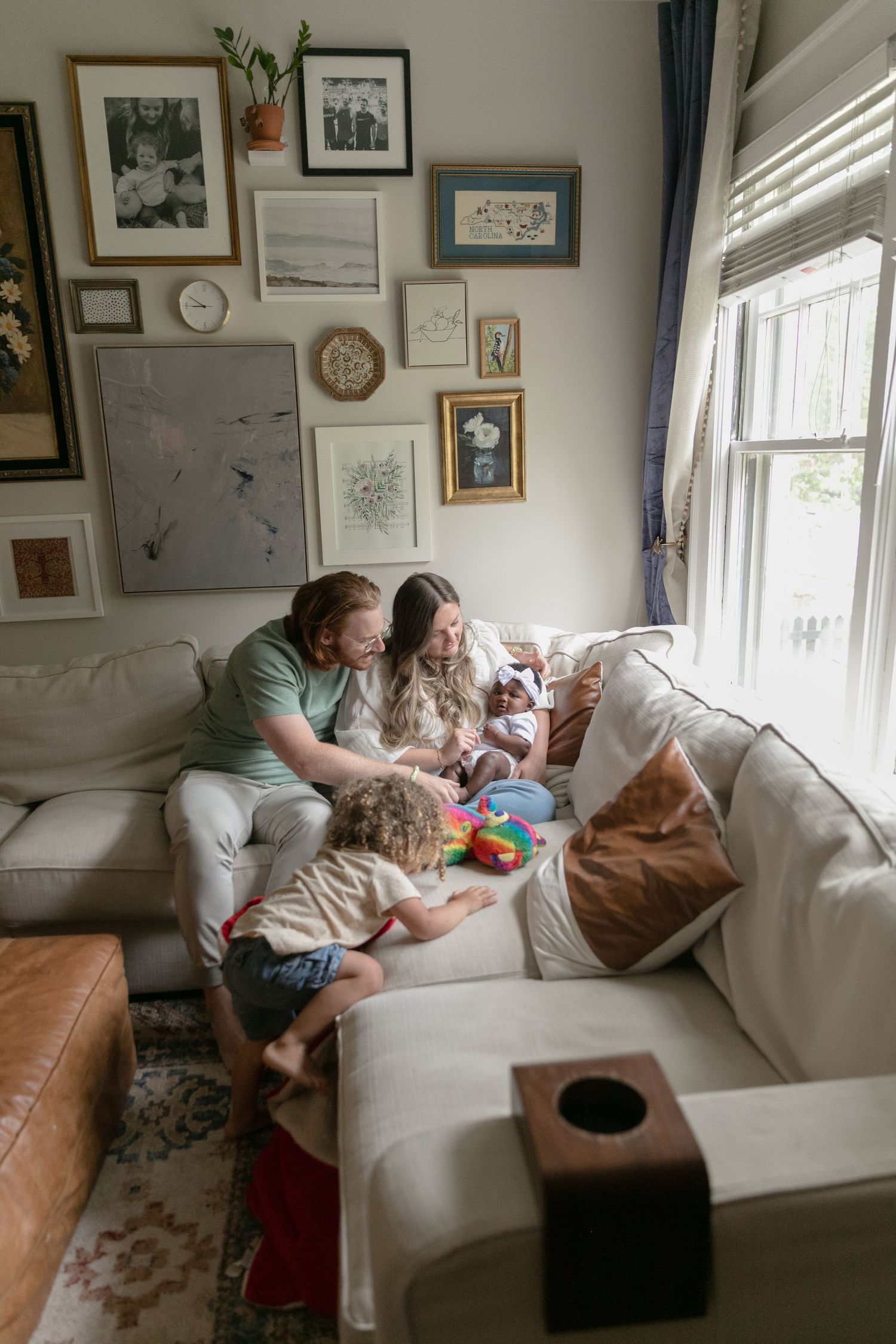 A cozy living room scene with family gathered on white couch beneath gallery wall of framed art.
