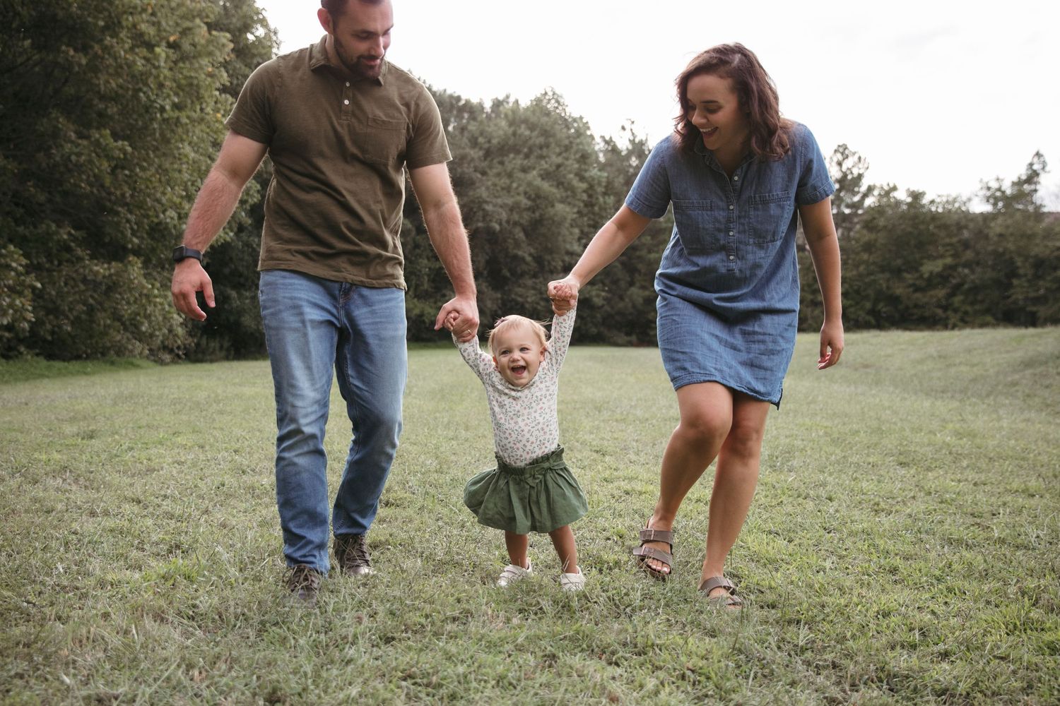 Parents help their toddler walk on grass during a fun family moment outdoors.