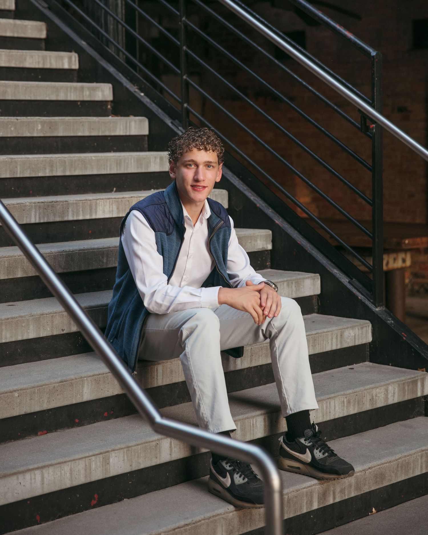 Person sitting casually on concrete steps with modern metal railings and wearing smart casual attire.