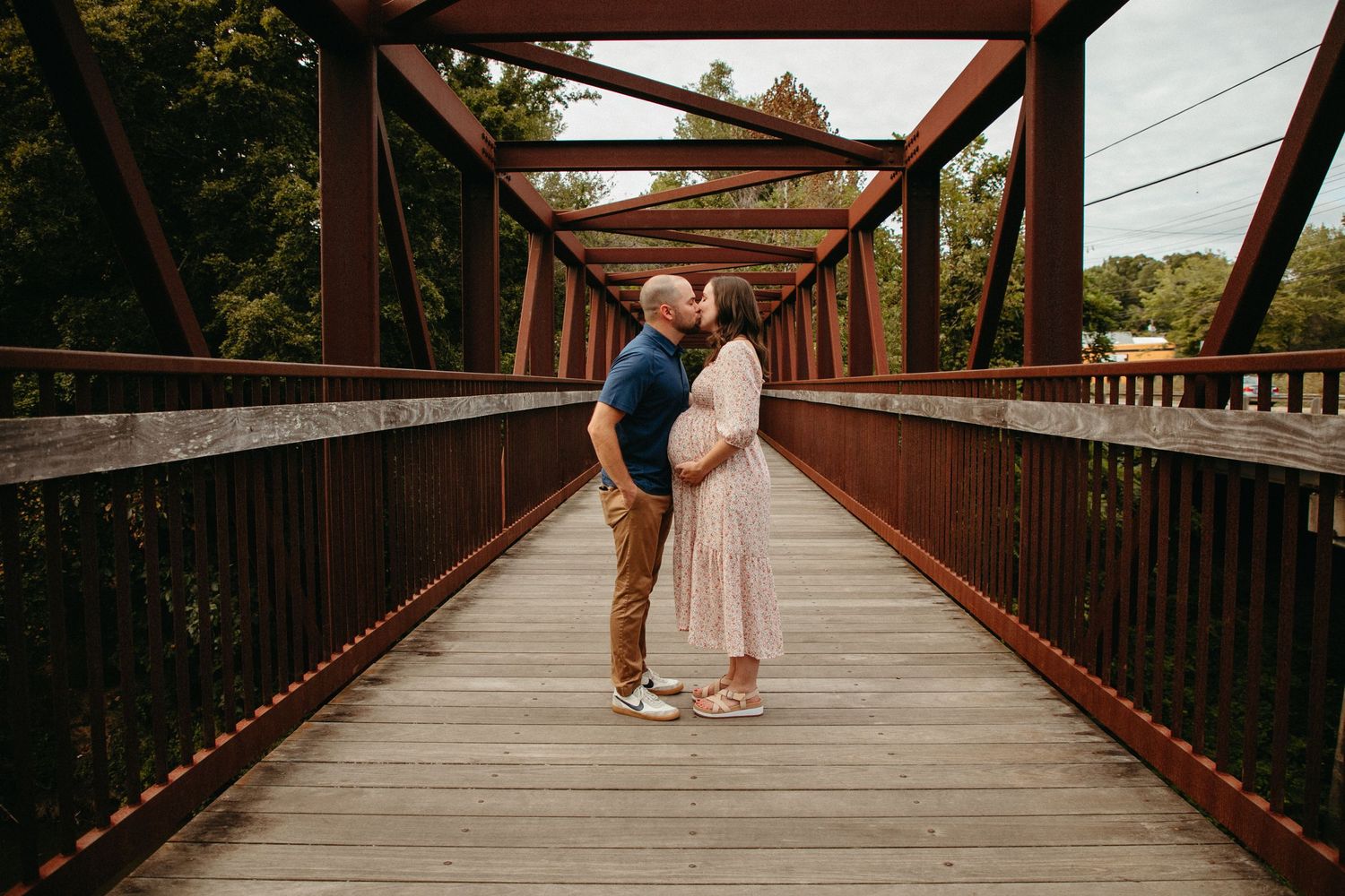 A couple shares an intimate moment on a wooden bridge with rustic metal framework.