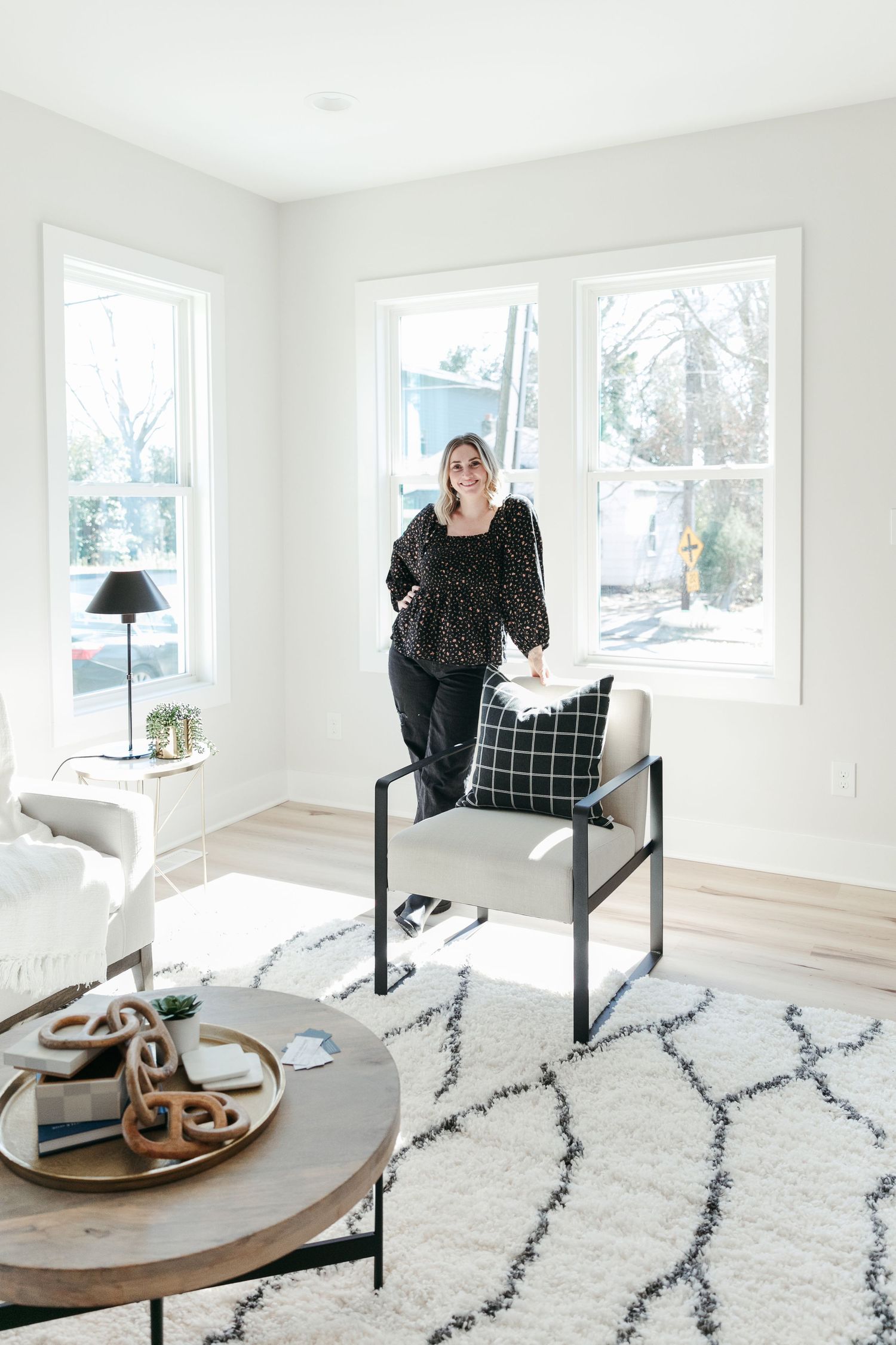 Contemporary living room with geometric rug, round coffee table, and large windows bringing in natural light.