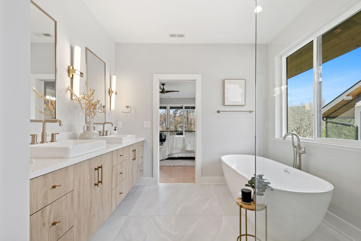 Luxurious modern bathroom with freestanding tub, light wood vanity, and gold fixtures.