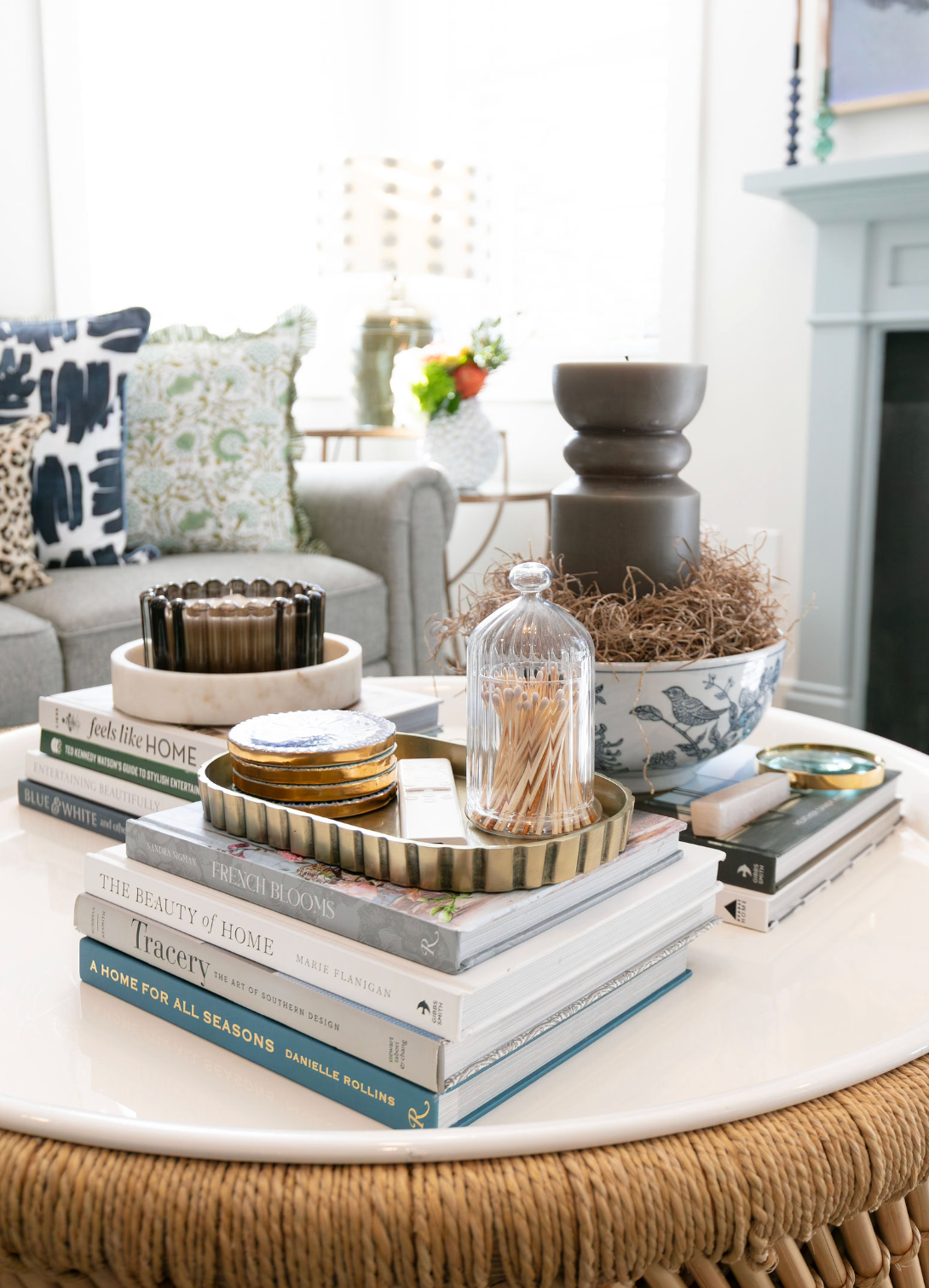 Styled coffee table with stacked books, glass cloche, candle, and decorative objects in a bright living room.