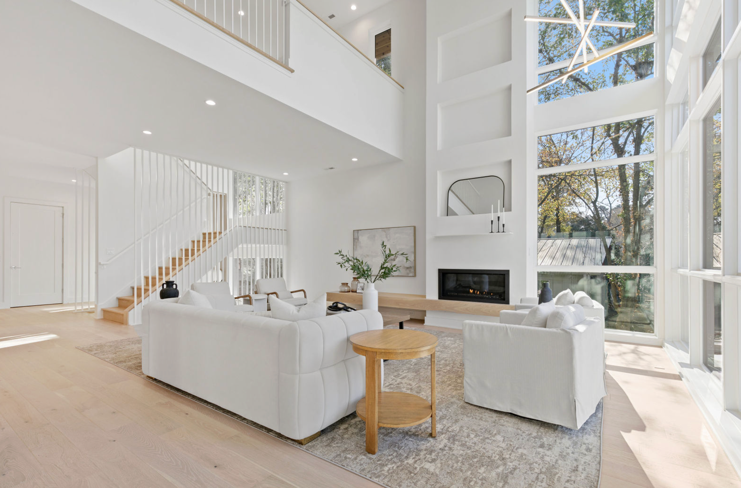 Bright modern living room with white sofas, high ceilings, fireplace, and large windows in an open-concept home.