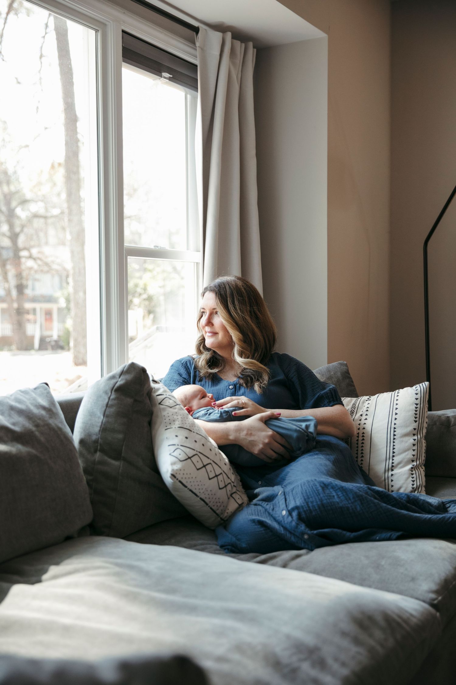 Cozy scene of relaxation with baby on grey sectional sofa near window.