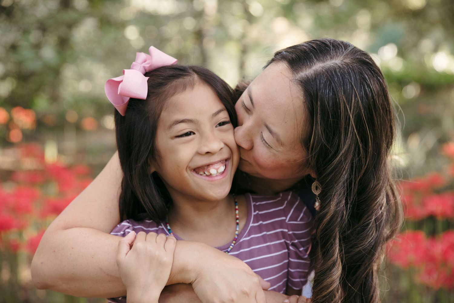Parent and child sharing affectionate moment outdoors with red flowers in background.