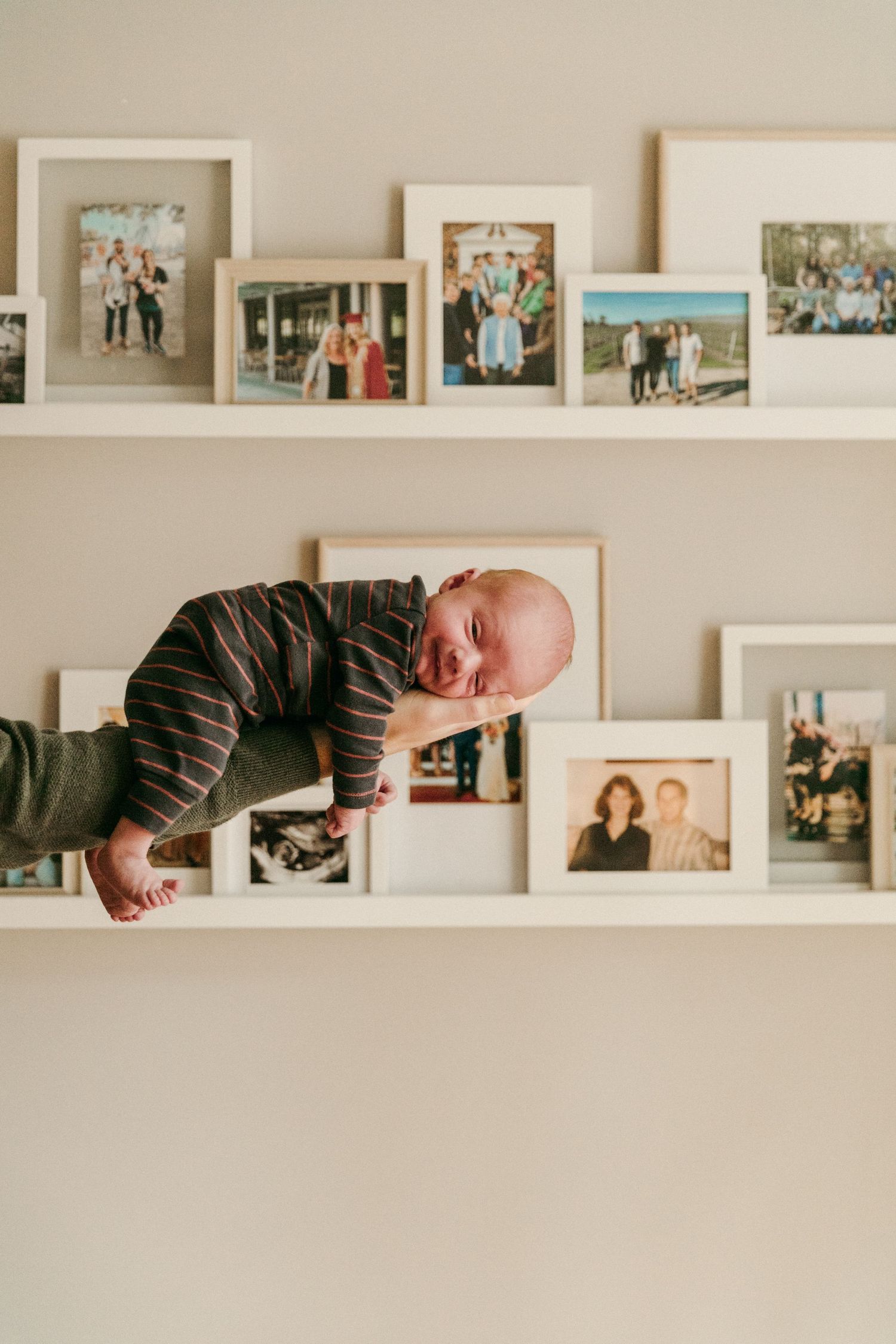 A nursery wall displays family photos on white floating shelves above a crib.
