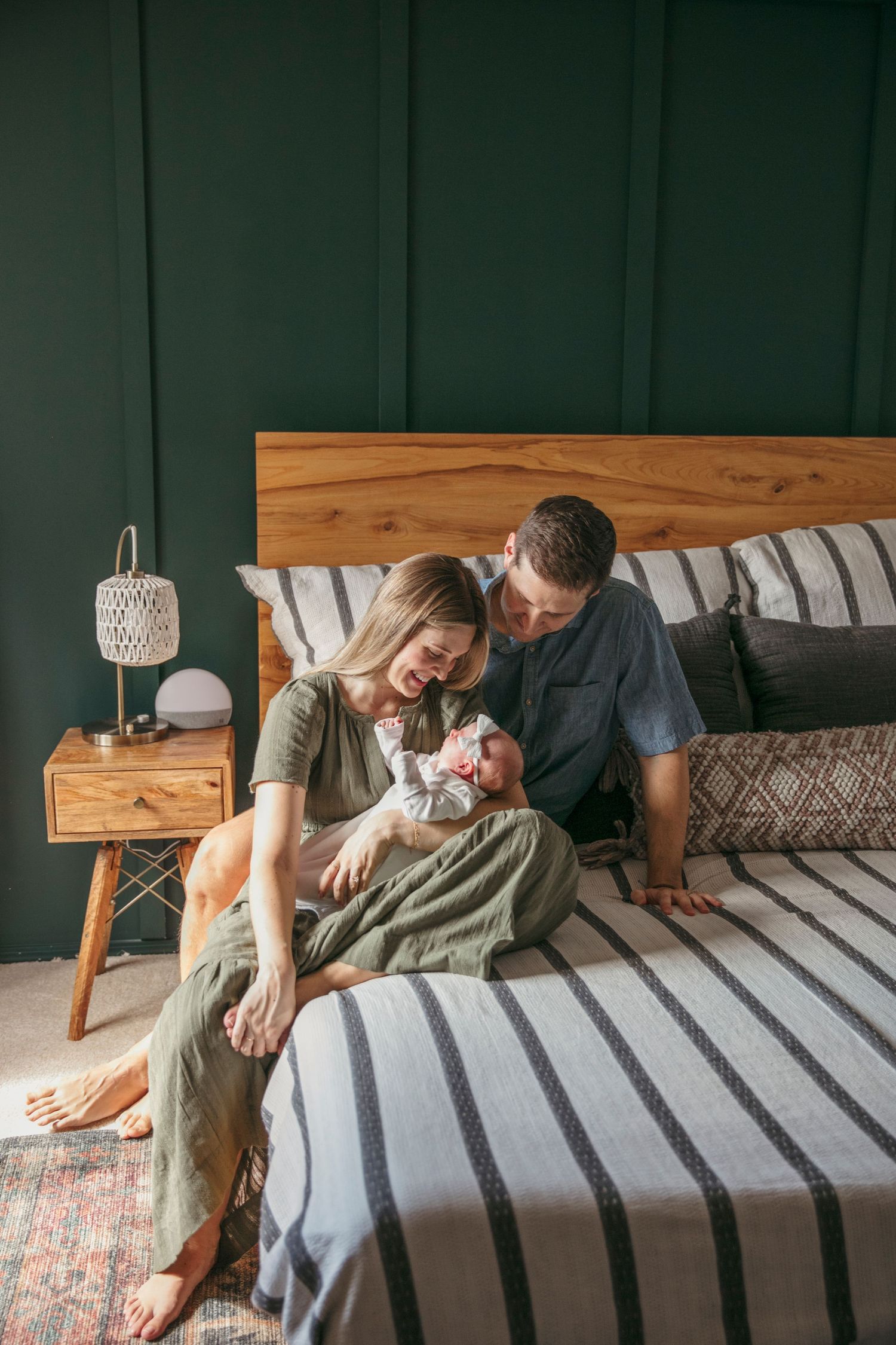 A family relaxes together with their newborn on a striped bed with dark green walls.