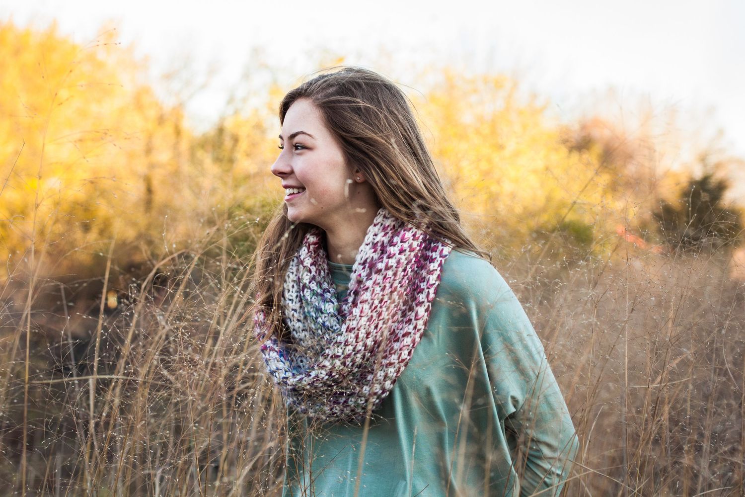 Person in mint green sweater and patterned scarf enjoying a sunny autumn day outdoors.
