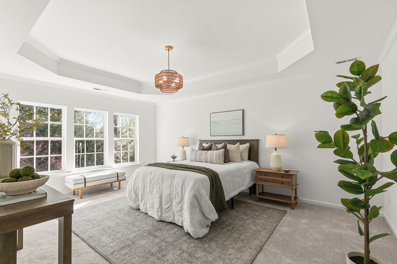 Elegant primary bedroom with tray ceiling, pendant light, neutral tones, large window, and plush area rug.