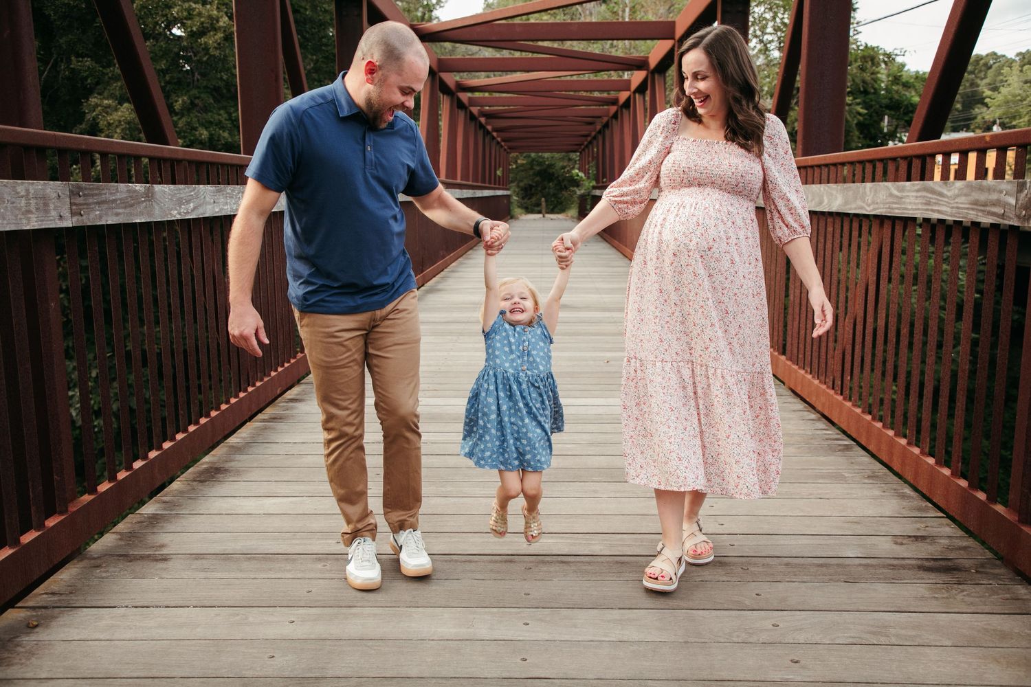 Family walking together on a wooden bridge surrounded by trees.