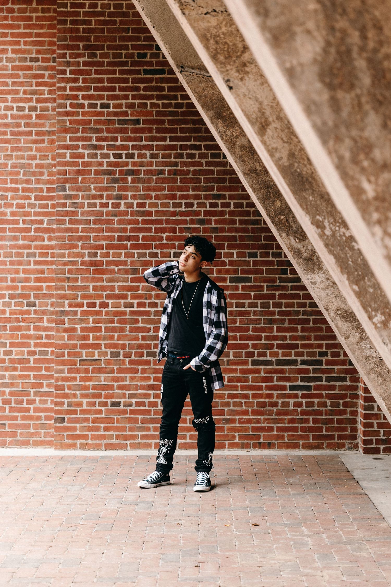 Urban fashion portrait against brick wall featuring plaid shirt and casual streetwear.