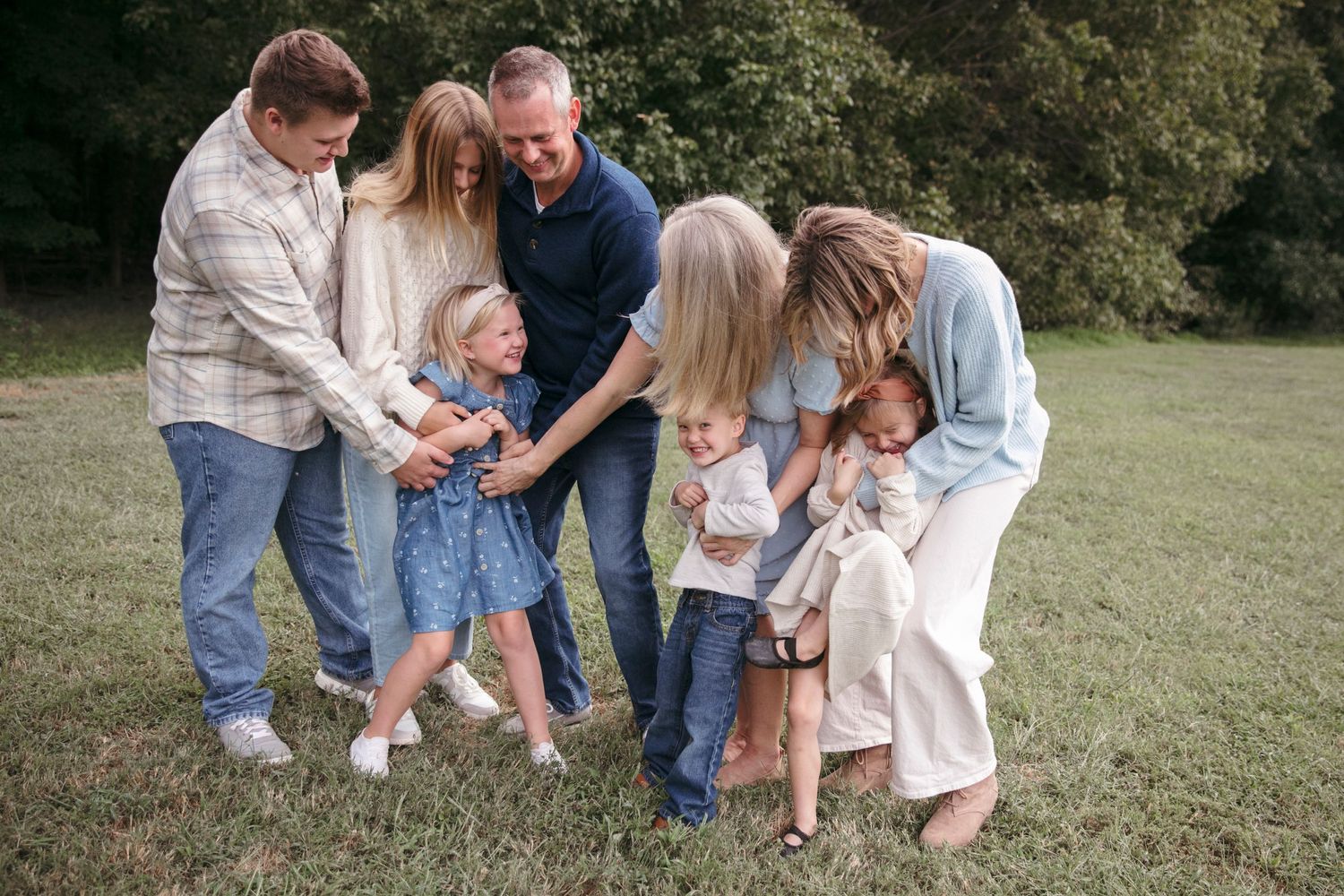 Family members bend down to share an intimate group moment on grass.