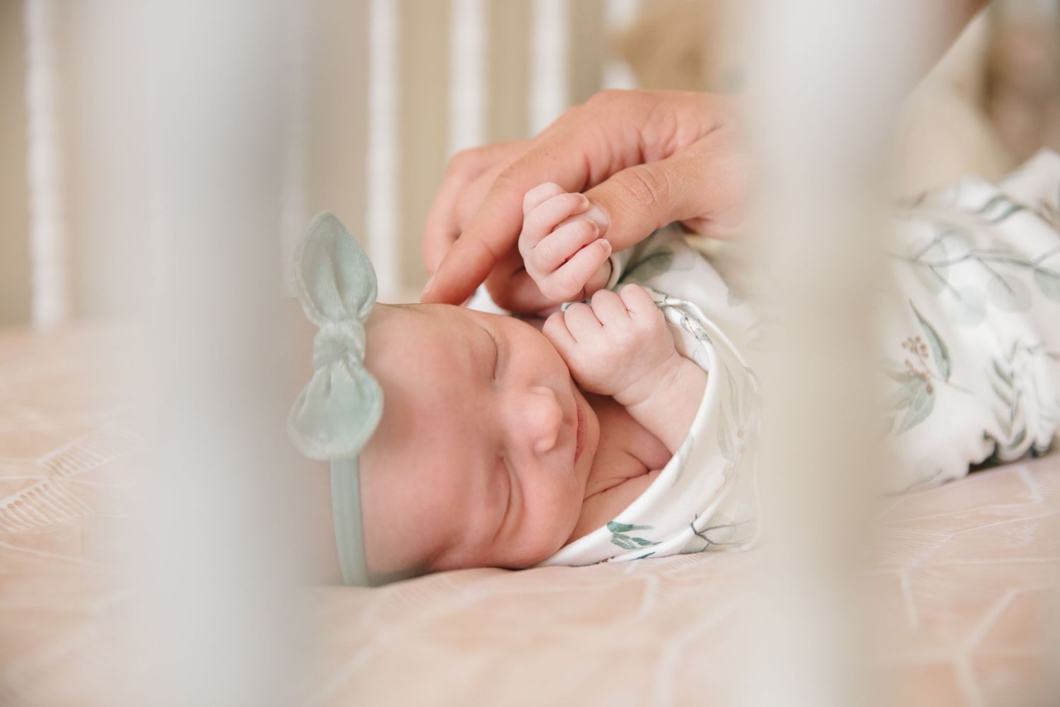 Close-up of tiny newborn baby fingers grasping against white fabric.