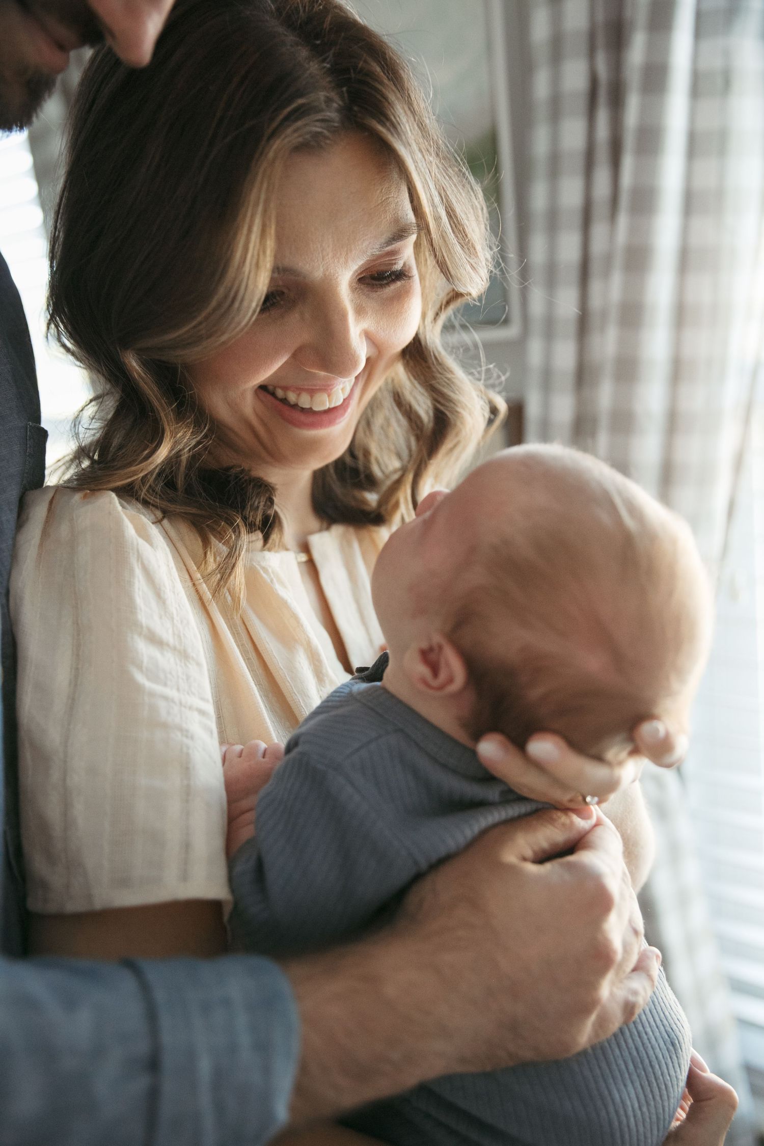 A tender moment between parent and baby as they share a joyful smile near a window with soft natural light.
