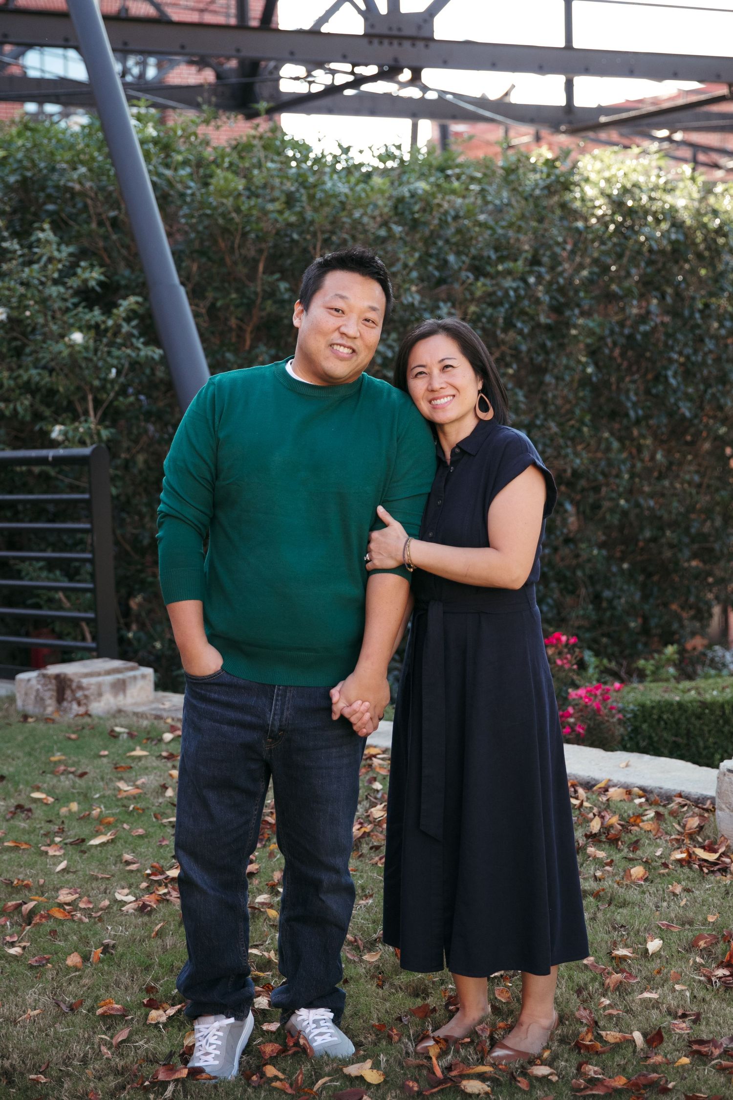 Couple in coordinating green and black outfits standing in garden setting.