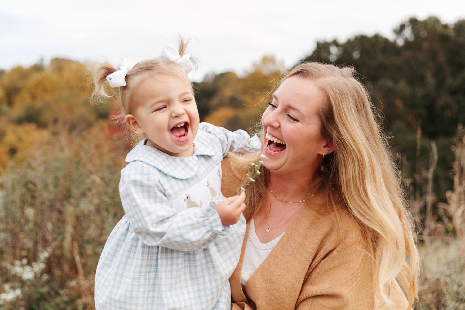 A joyful outdoor portrait of parent and toddler laughing together in a natural autumn setting.