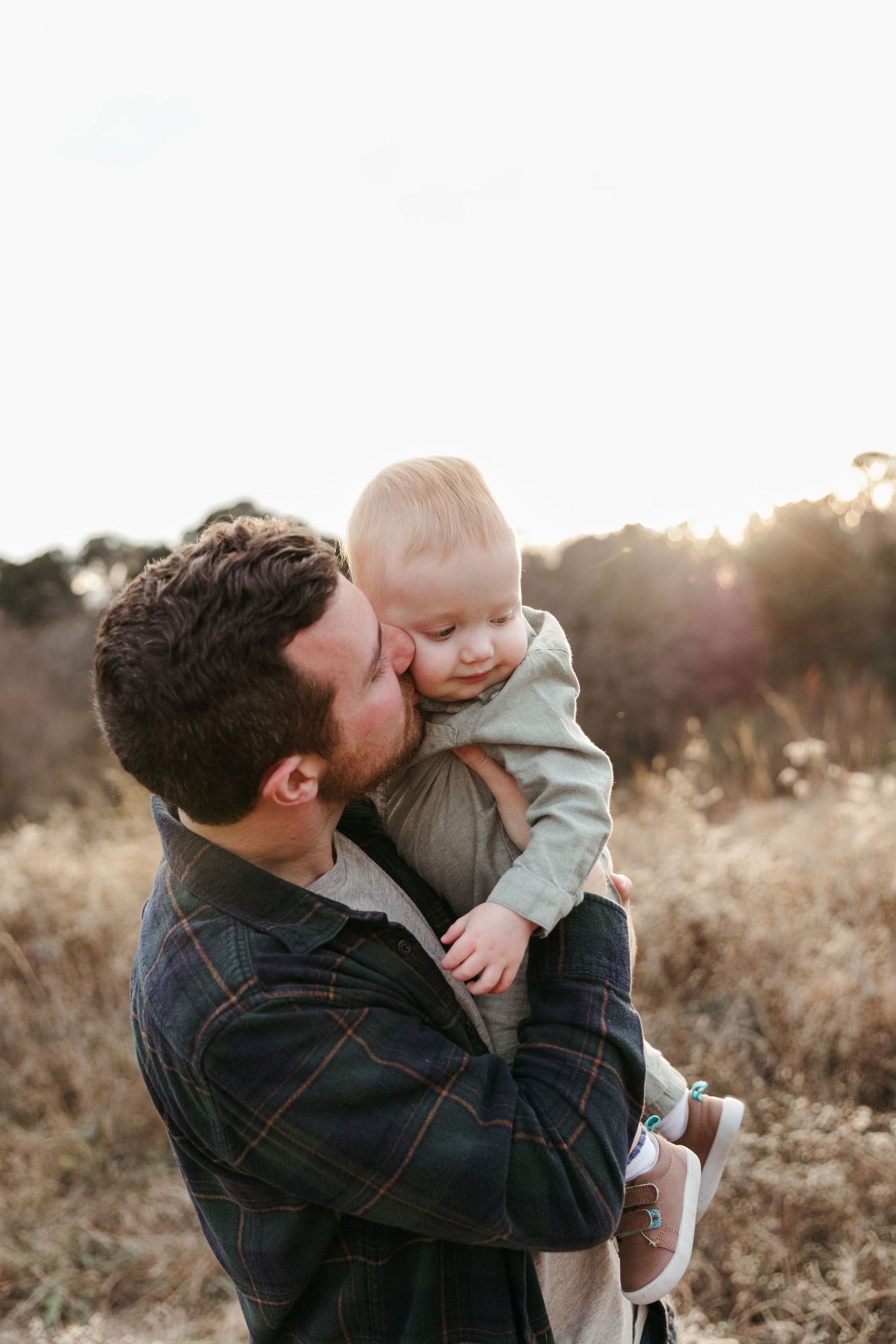 A tender moment between parent and baby captured in golden light at sunset in a field.