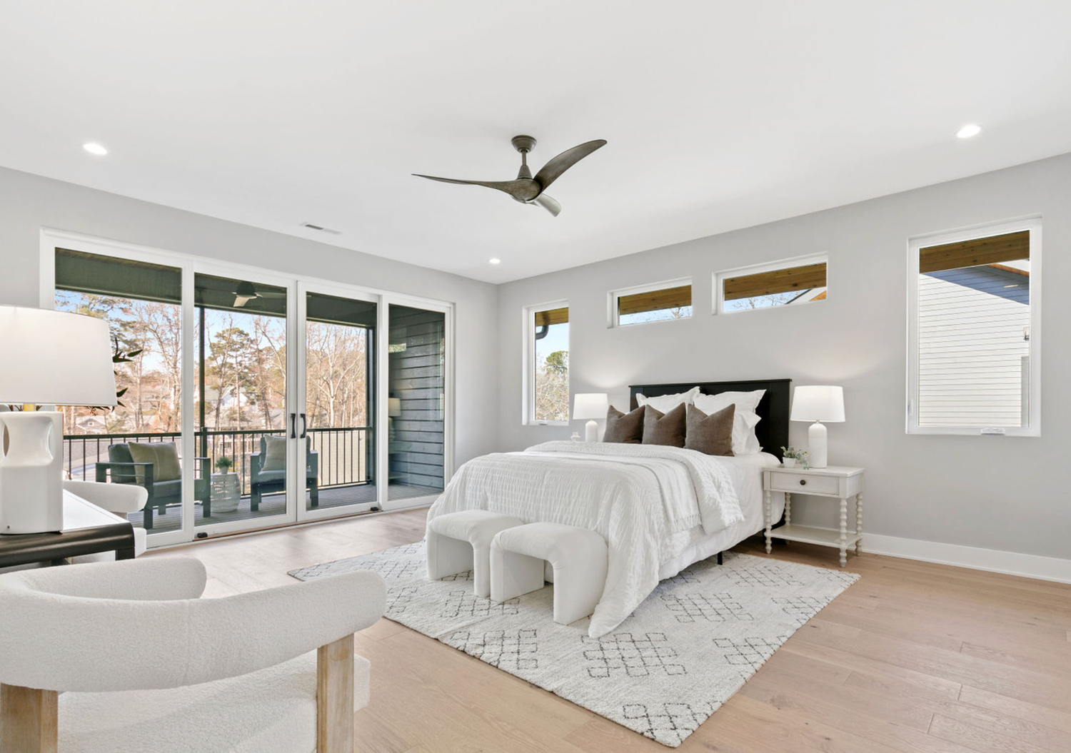 Modern master bedroom with gray walls, ceiling fan, sliding glass doors to balcony, and light hardwood floors.