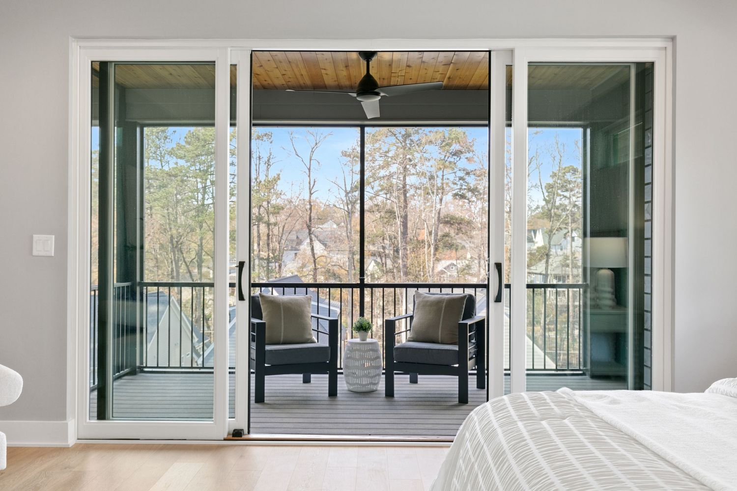 Large glass sliding doors open to a screened balcony with forest views and outdoor seating.
