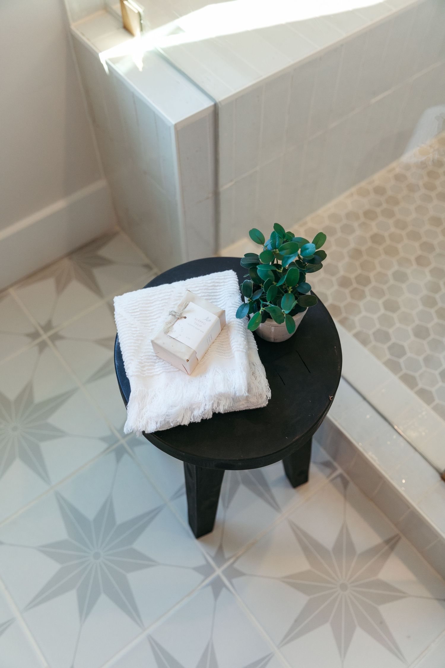 Decorative black table with white towels and green plant on star-patterned tile floor.