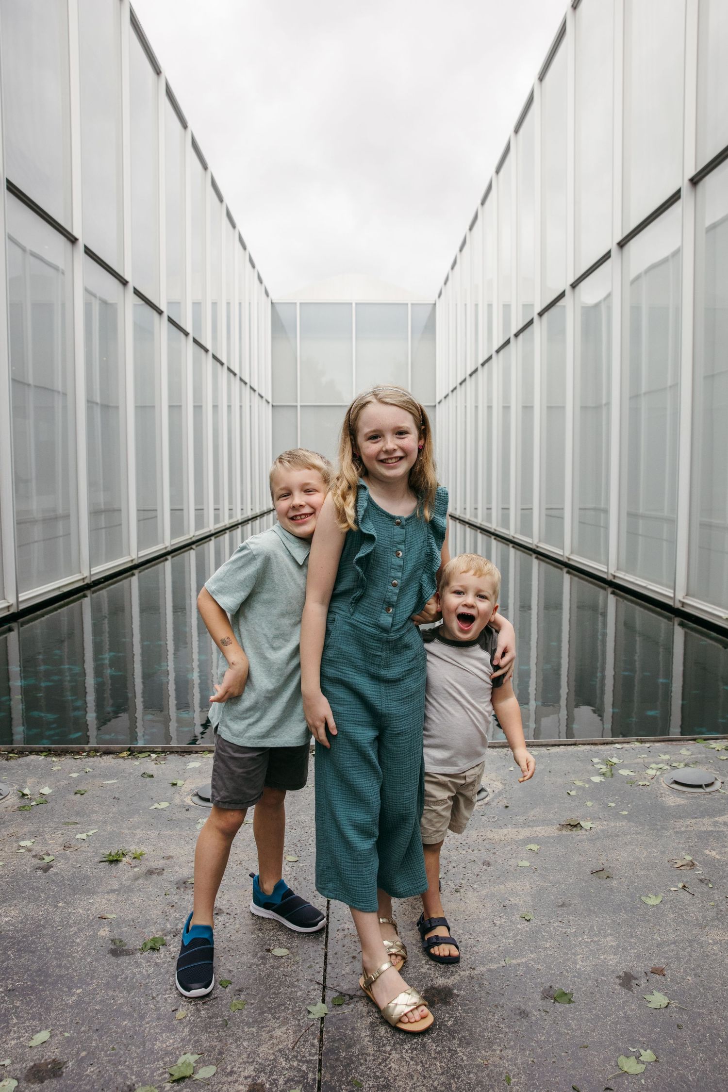 Three children posing playfully in a modern corridor with metallic walls.