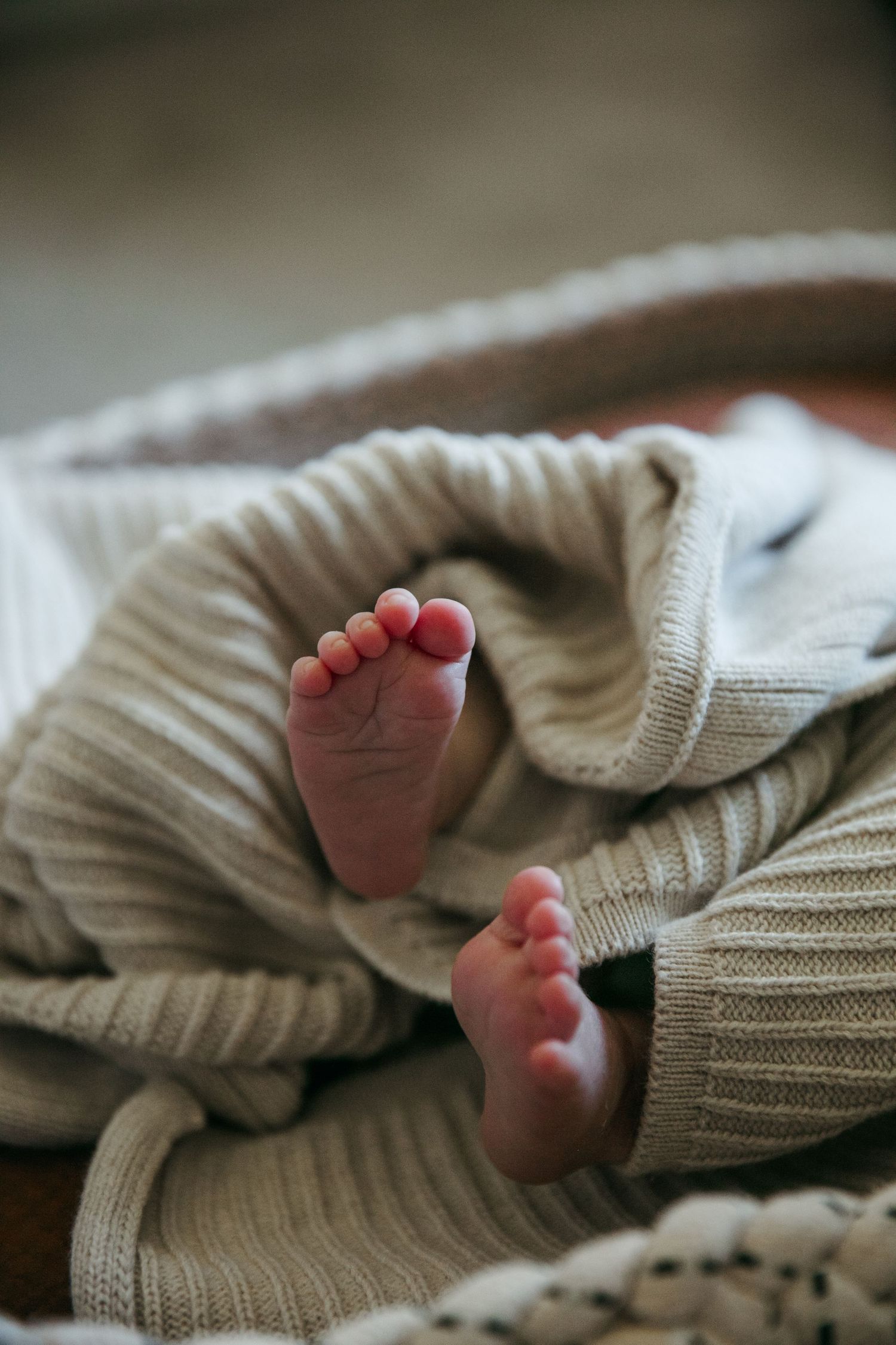 Tiny baby feet peeking out from under a cozy knit blanket in soft focus.