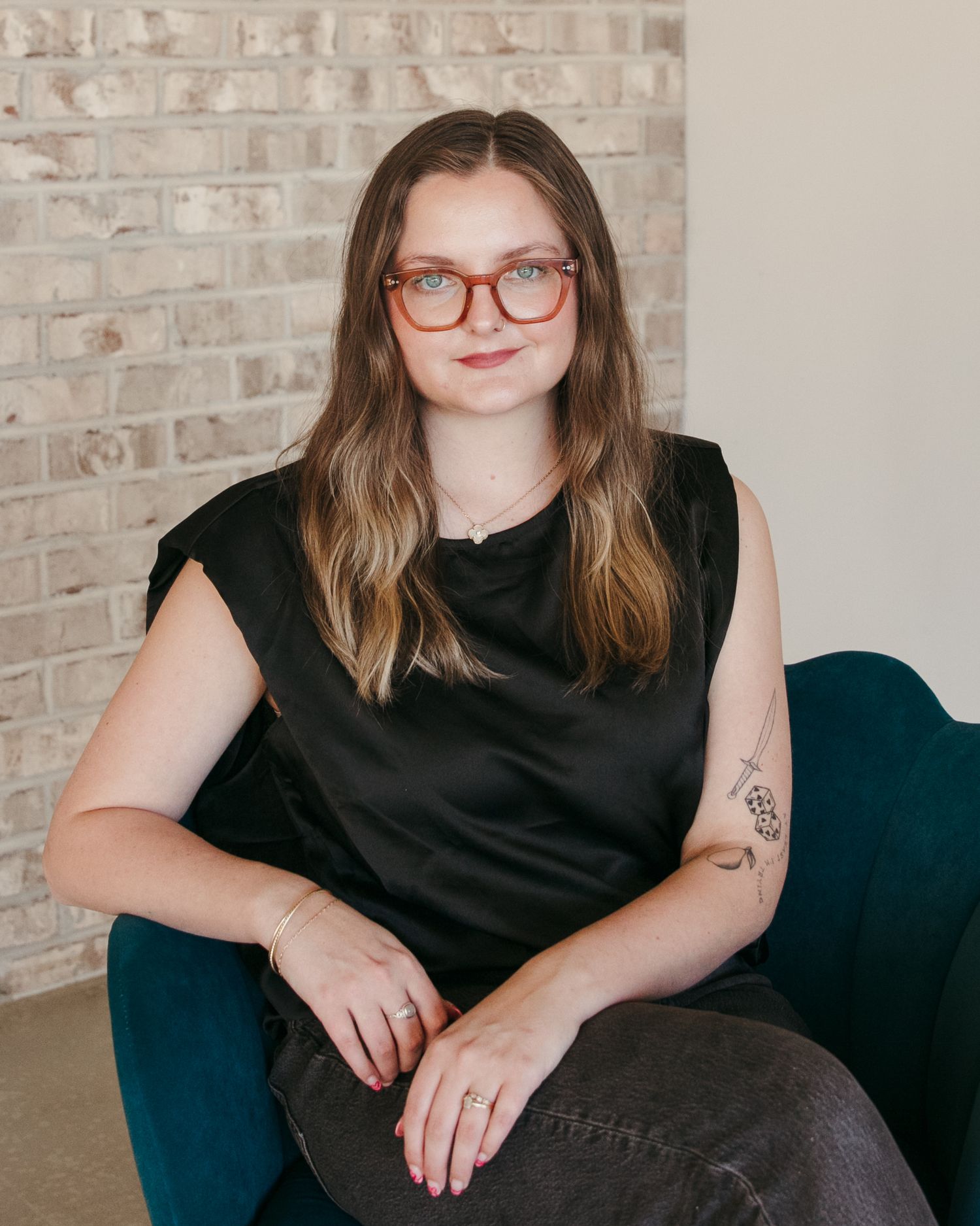 Professional portrait against brick wall wearing black top and red glasses.