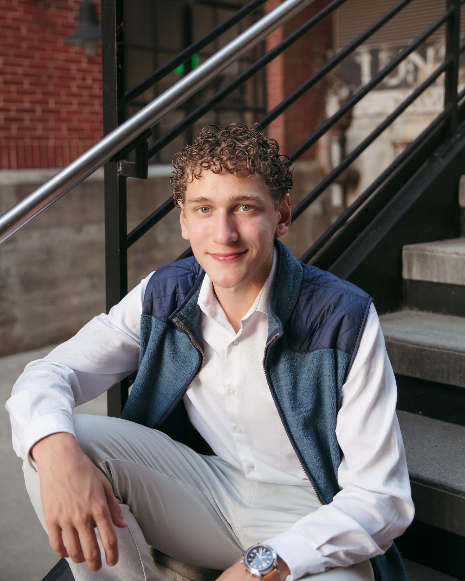 Person in navy vest and white shirt sitting on outdoor steps.