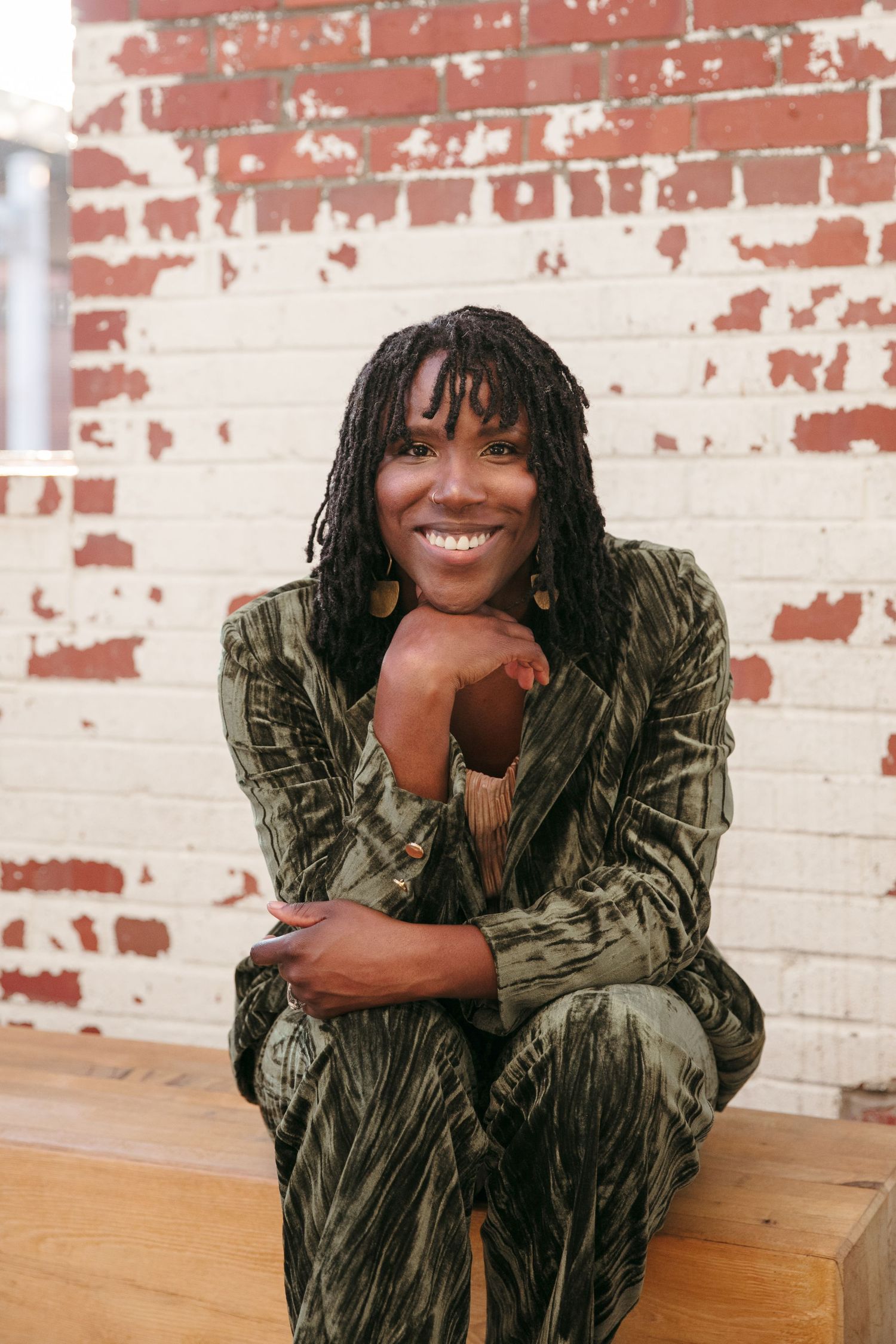 Person in velvet jacket reclining on wooden floor against painted brick wall.