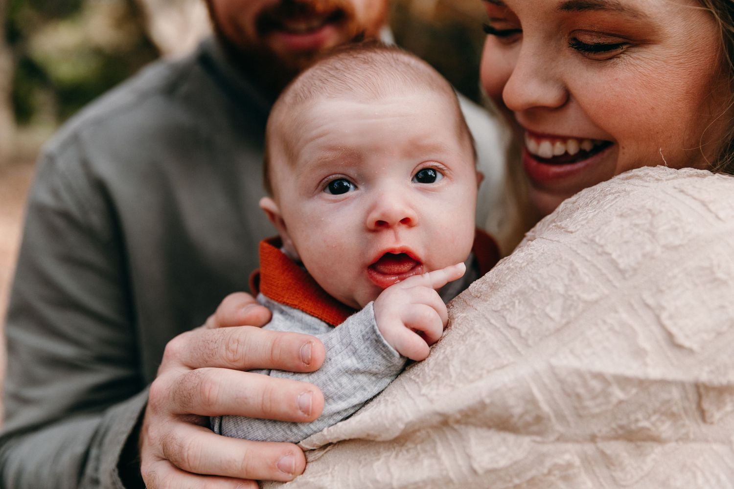 Baby being held and cuddled by adults in an outdoor setting.